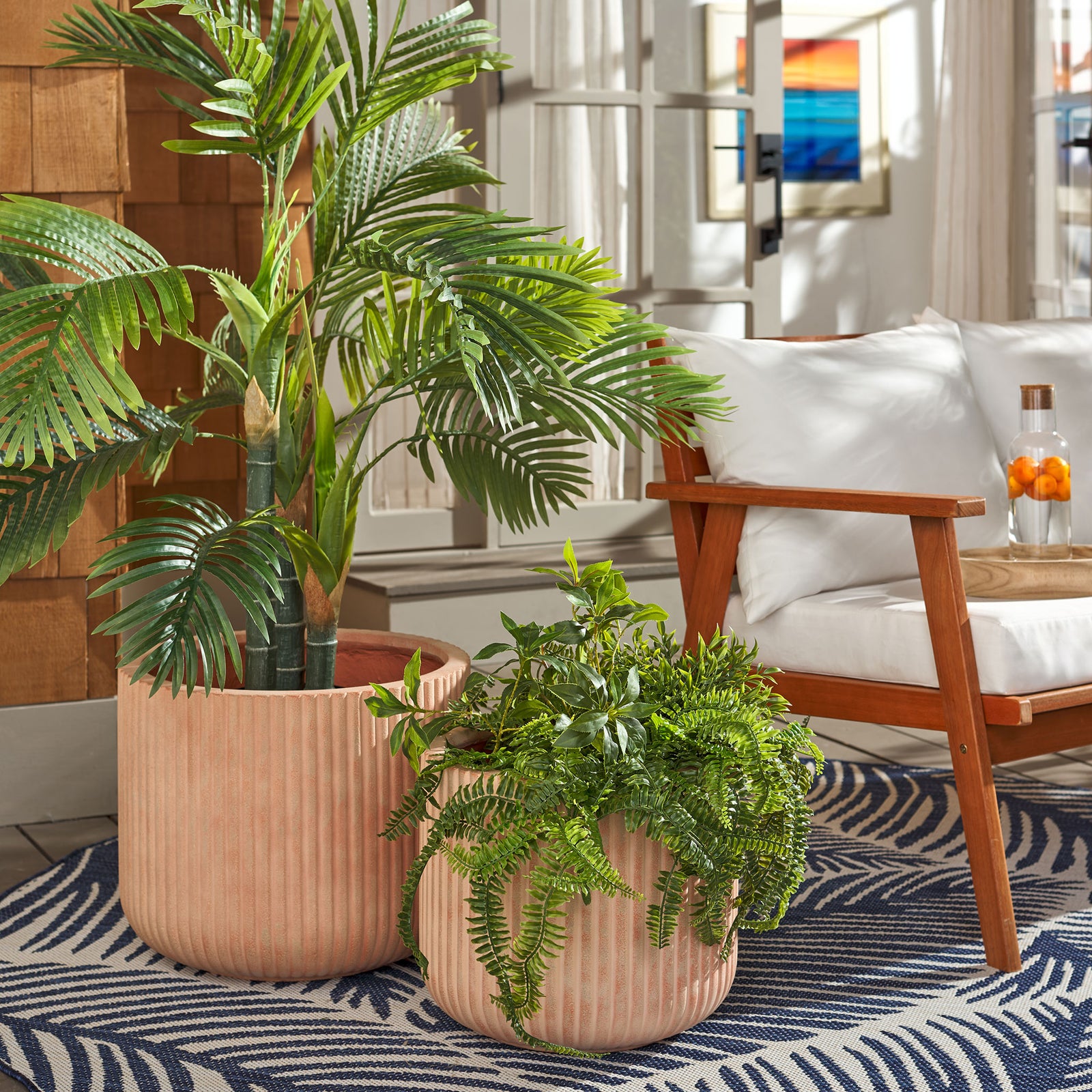 Two fluted terracotta planters bring warmth to a palm and trailing greenery near a cushioned chair. || PAT1532D-SET2 || front_angle_room