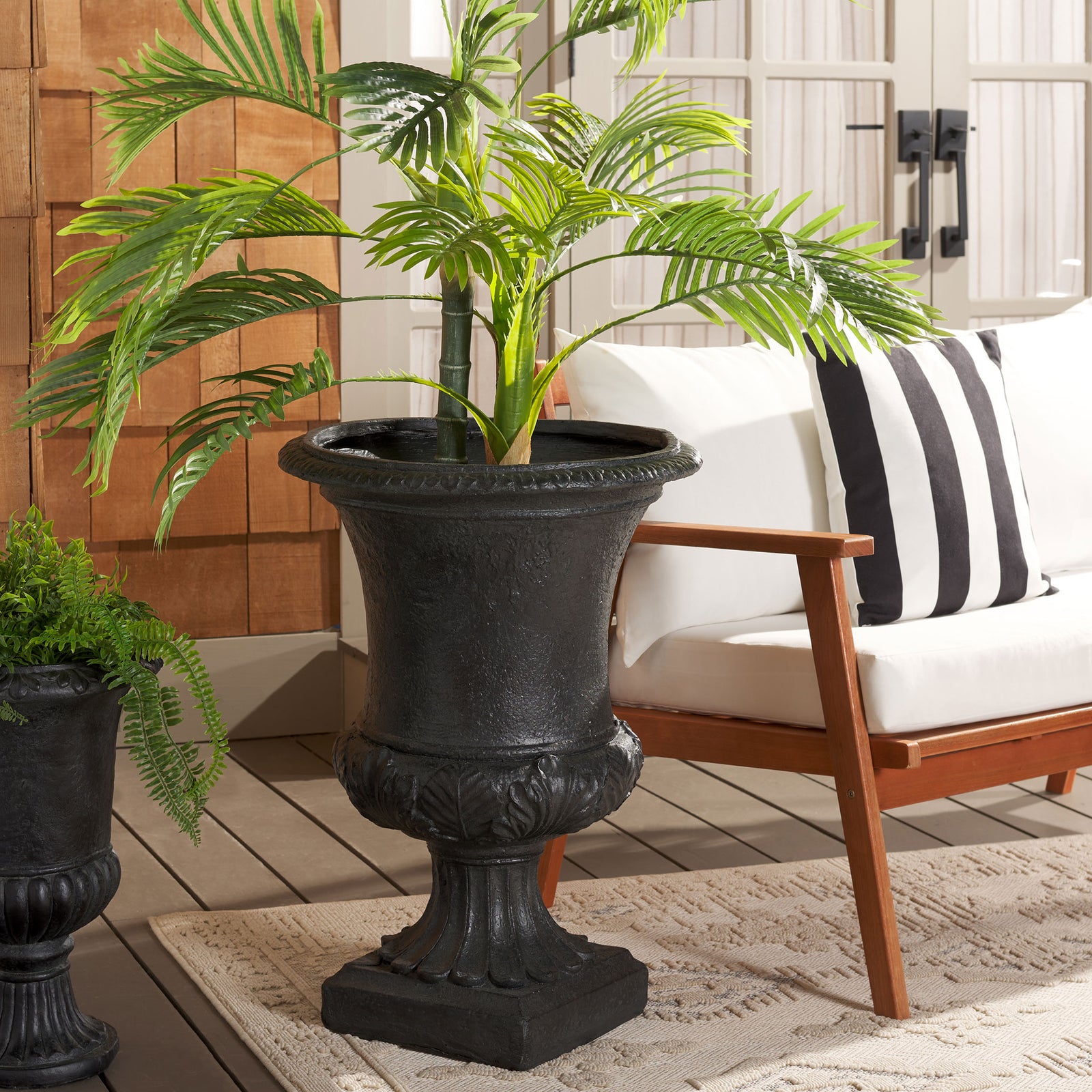 The black urn planter elevates leafy greenery beside a patio chair. || PAT5038E || front_room