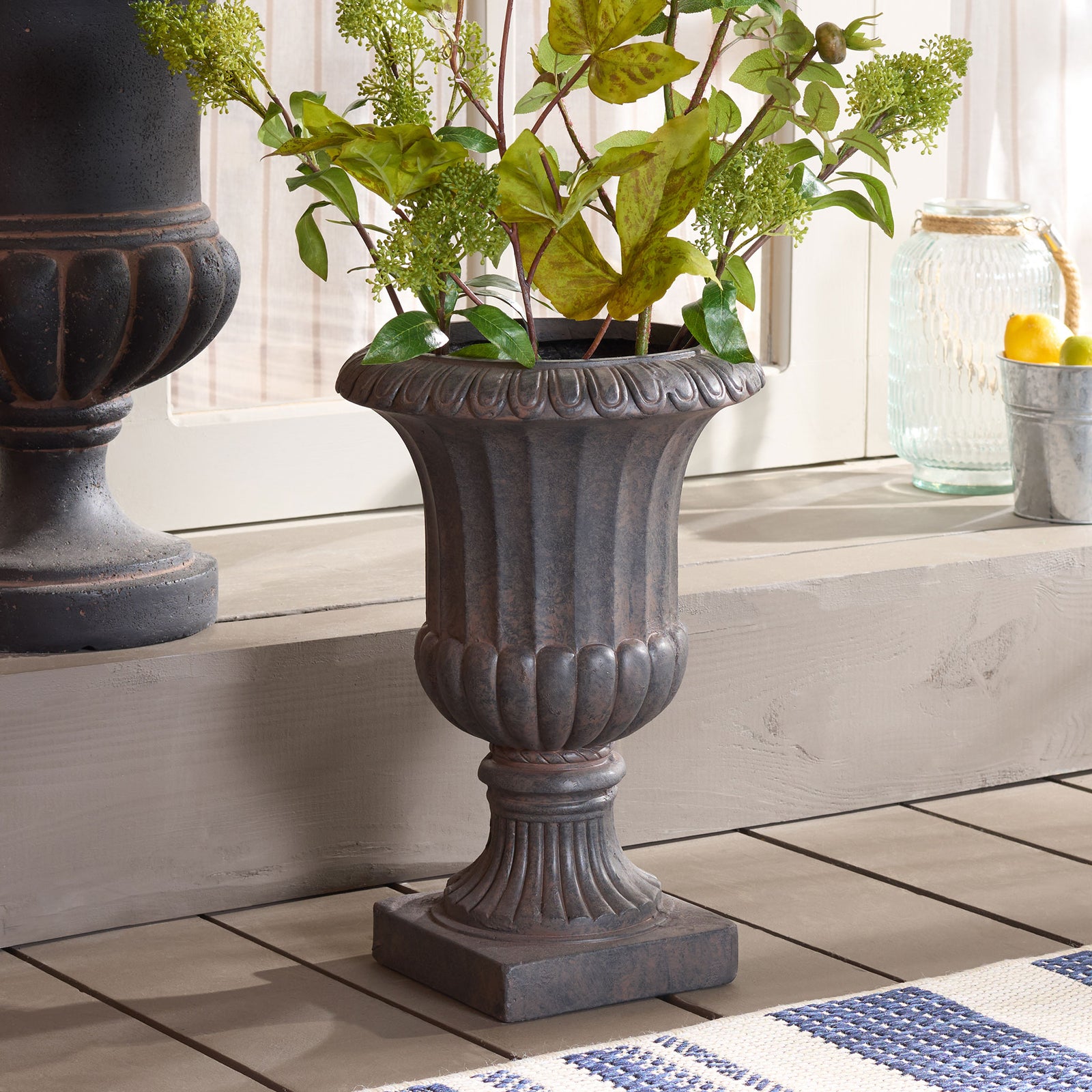 Green foliage rises from the brown fluted planter, adding an elegant focal point to a tiled setting. || PAT5045B || front_angle_room