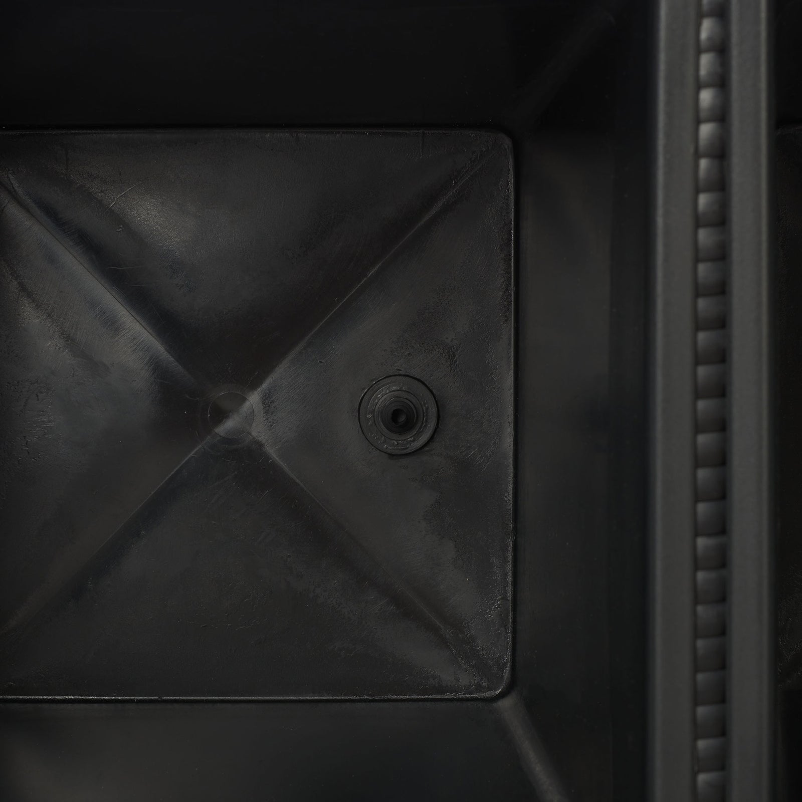 A circular drain opening is molded into the base of a black planting bin. || PAT7705A || detail_studio