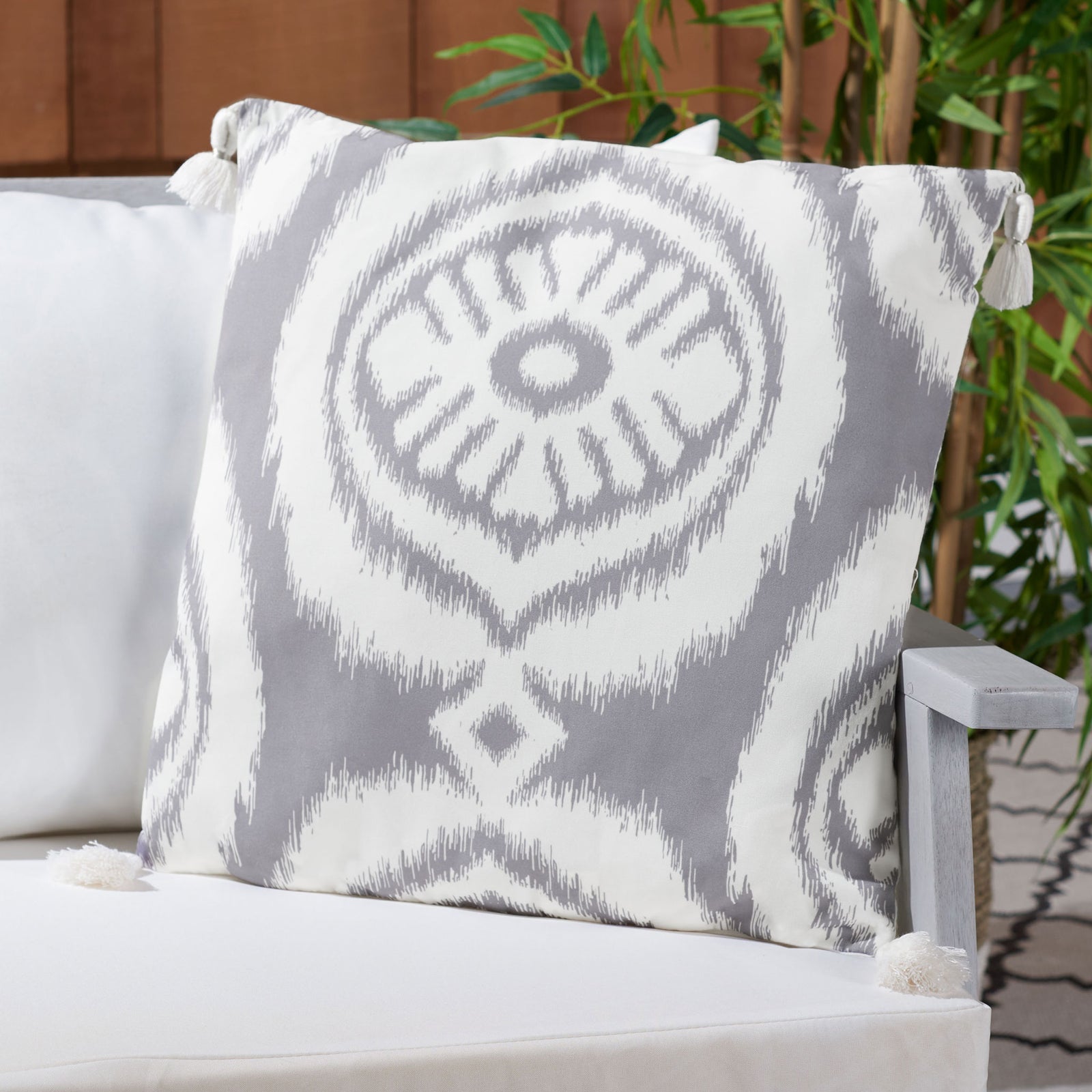 A gray-and-white patterned pillow with corner tassels adds contrast to a cushioned outdoor bench || PPL261A-1818 || front_room