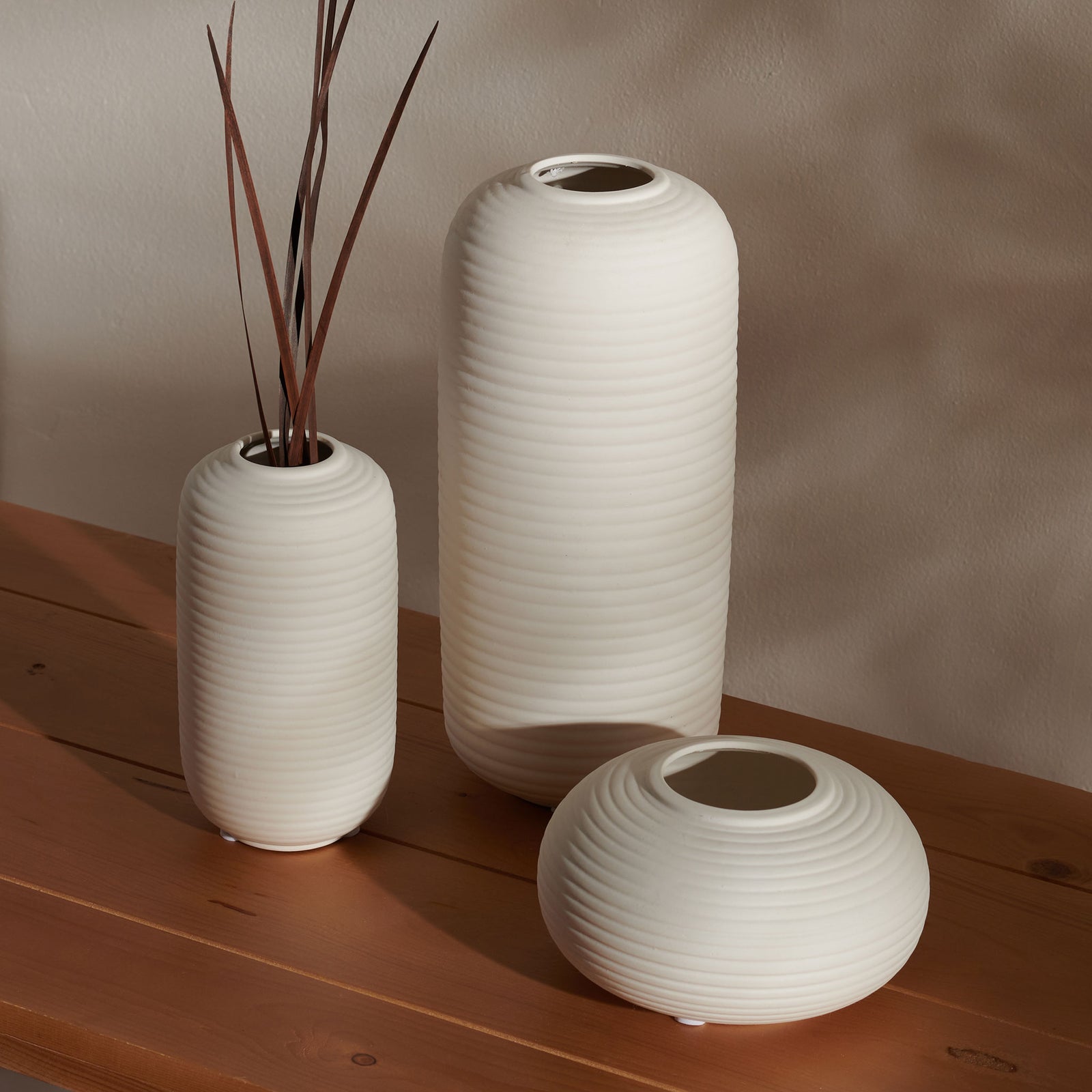 Three ivory ceramic vases bring soft, ribbed texture to a wood tabletop, with branches in one vessel || RDC4016A-SET3 || front_angle_room