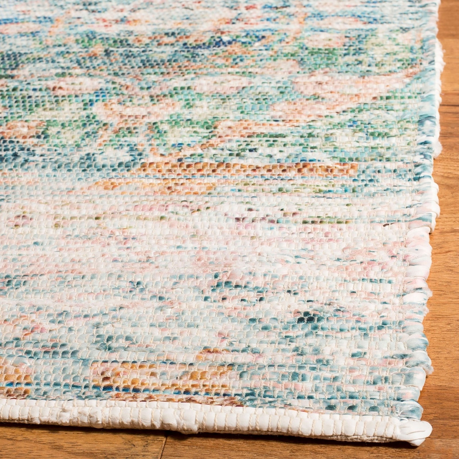 Close-up of turquoise and peach rug's textured weave and neatly bound corner on a wood floor || SFN563A-5 || corner_room