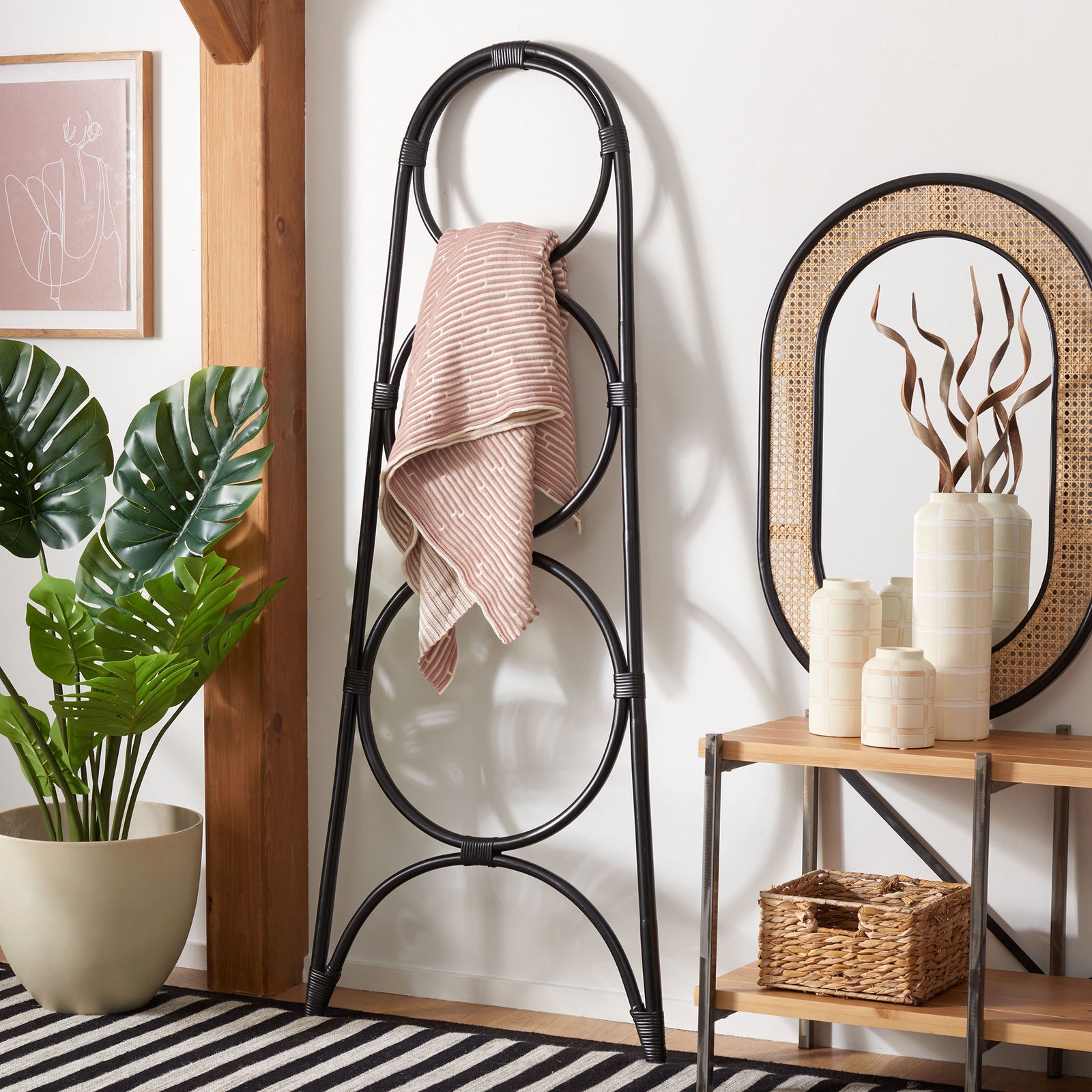 A blush striped towel hangs from the black rattan rack's three-tier circular frame. || STG6501B || front_angle_room
