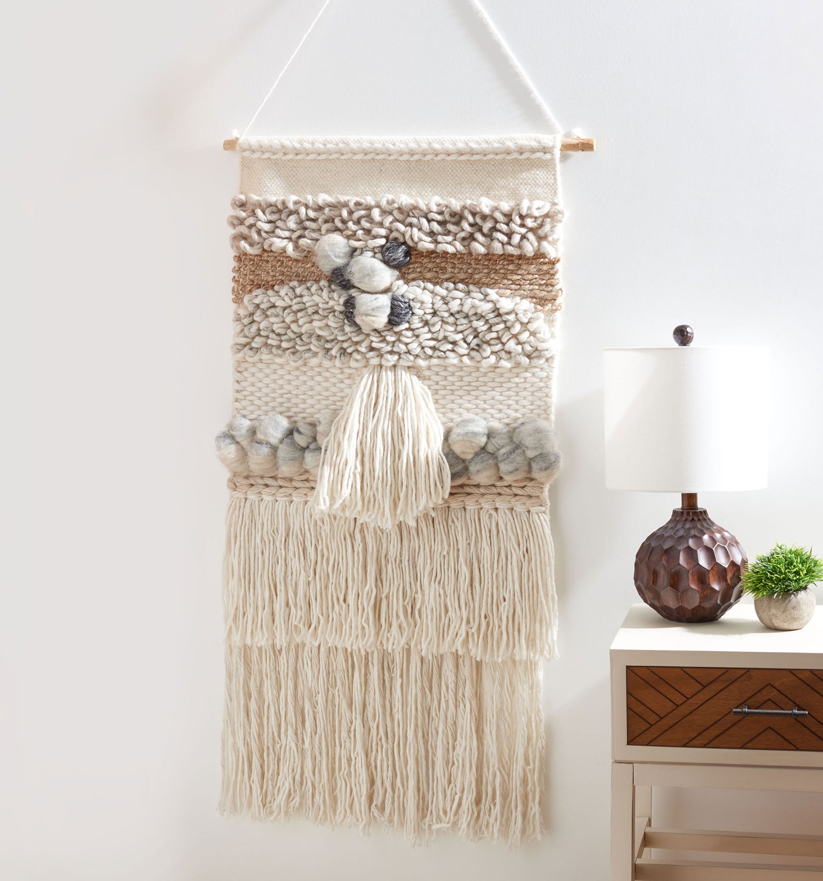 Ivory and gray wall tapestry brings plush bobbles, a center tassel, and layered fringe to a neutral palette. || SWA144-2 || front_room