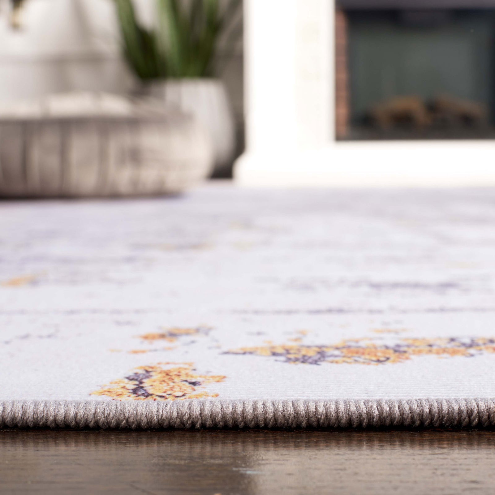 Close-up of finished edge and thin profile for easy door clearance on a patterned gray and gold rug. || TAC863F-5 || detail_room