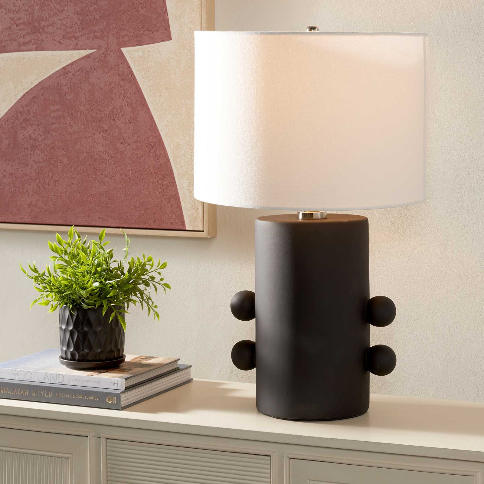 Warmly lit off-white shade crowns a matte black ceramic base with playful side spheres. || TBL2008A || front_angle_on_room