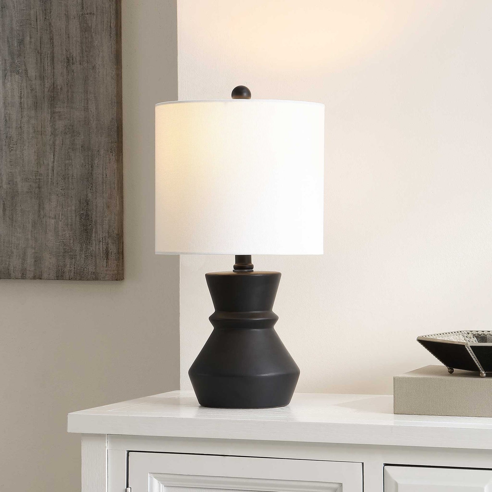 Ambient glow highlighting a sculpted black ceramic base and clean white drum shade. || TBL4515A || front_angle_on_room