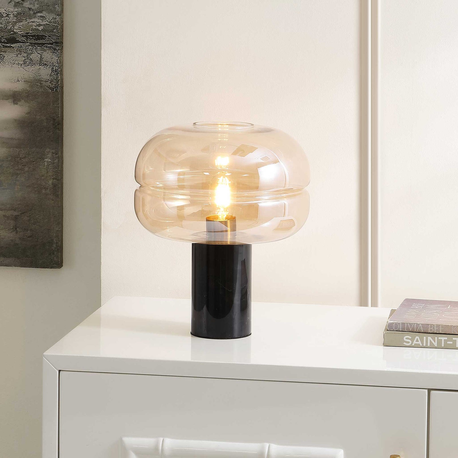 Amber glass shade casts a cozy glow from a sleek black marble base, elevating modern decor. || TBL4518A || front_angle_on_room