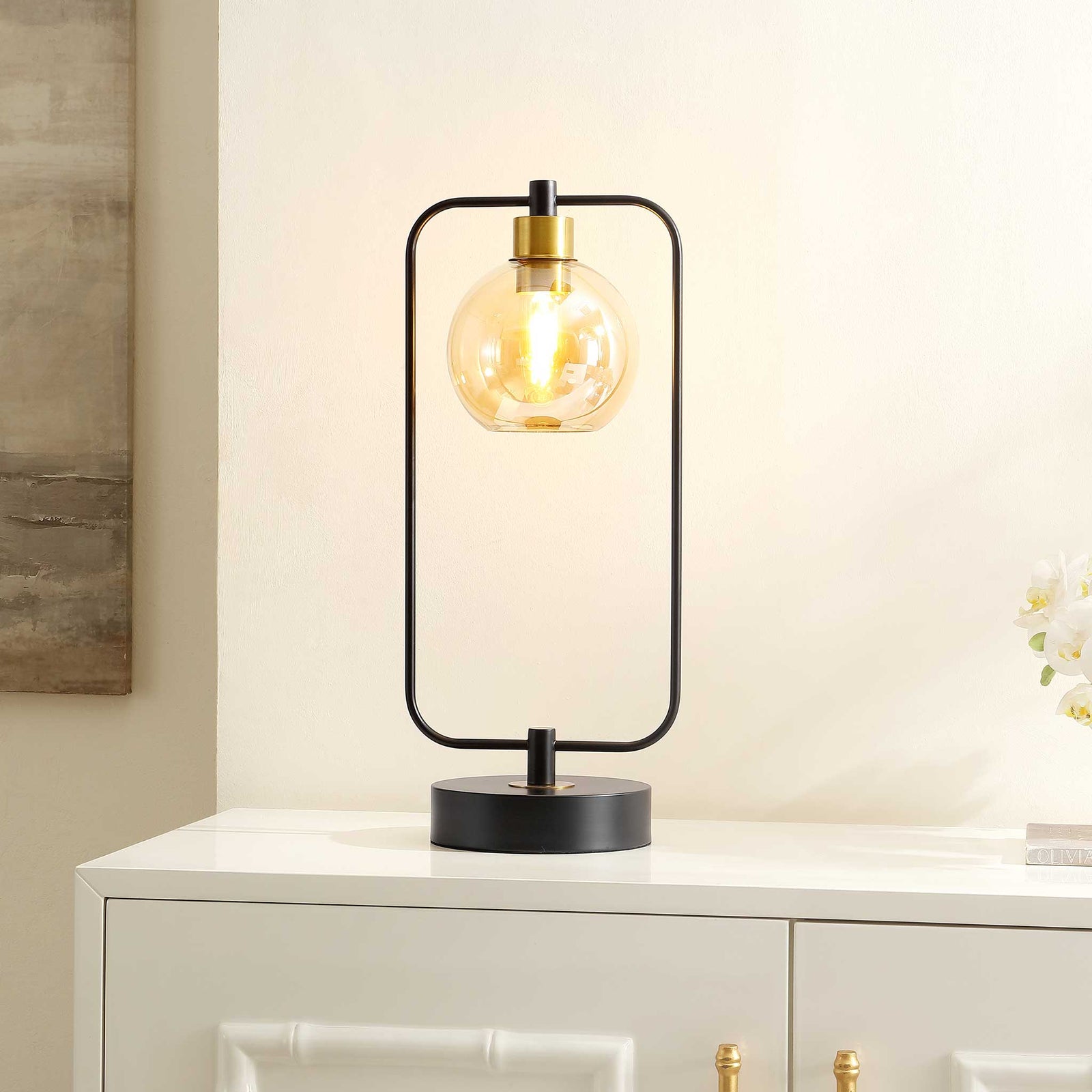 Warm amber glow shines through the globe while the black frame brings chic, modern impact || TBL4524A || front_angle_on_room
