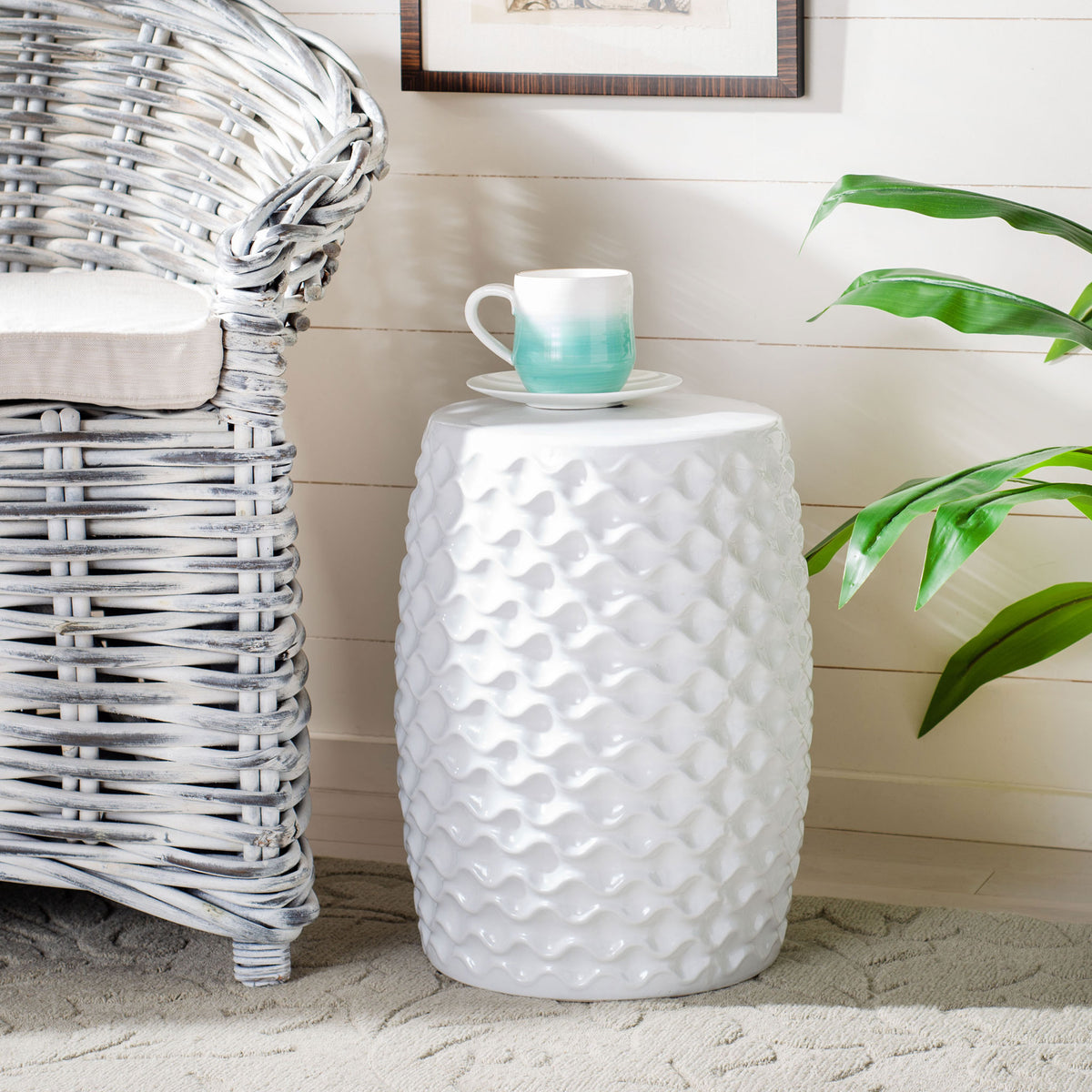 Sculpted white ceramic garden stool serves as a compact side table beside a wicker chair || ACS4579A || front_angle_room