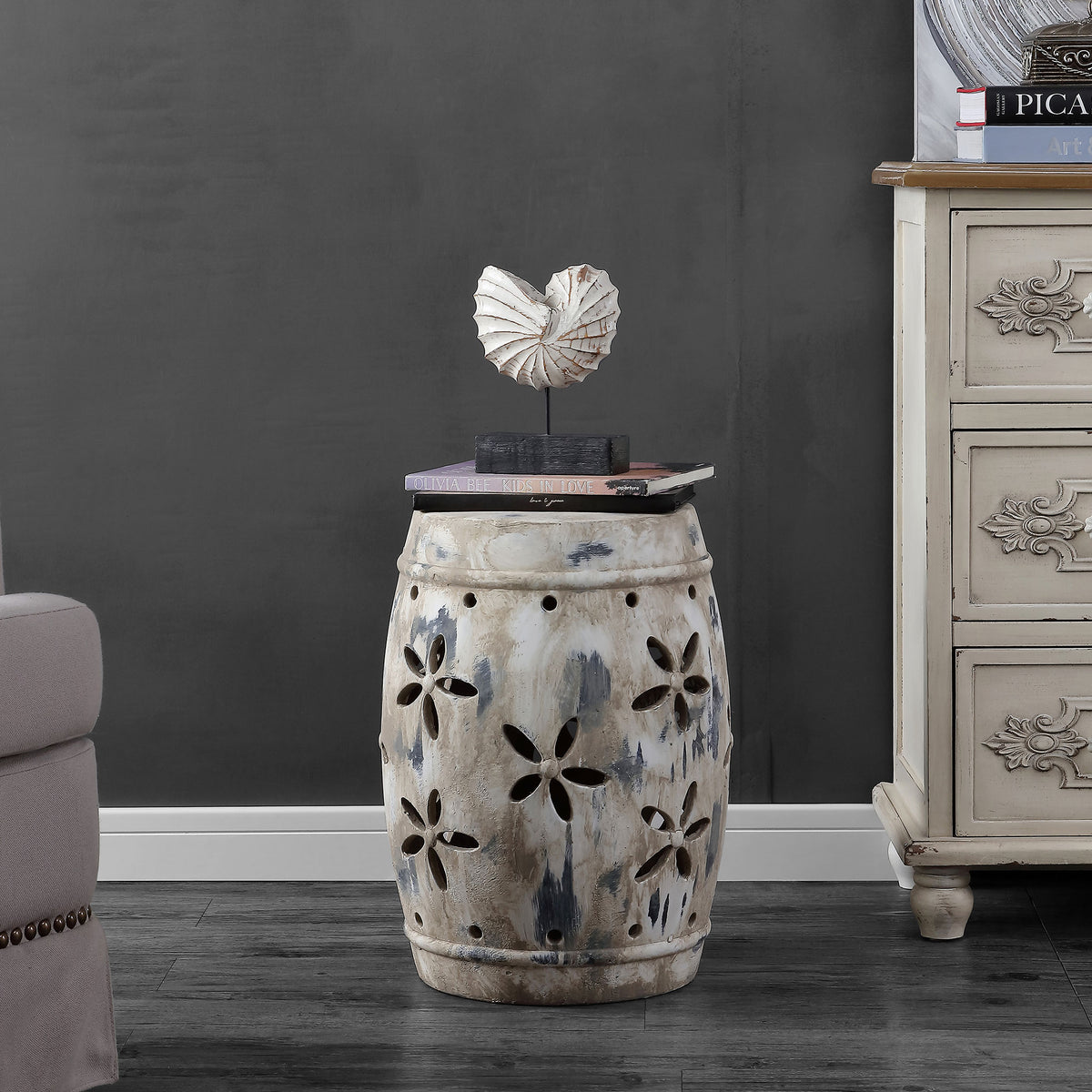 An antique cream ceramic stool adds a weathered floral accent beside living room furniture || ACS4589A || front_room
