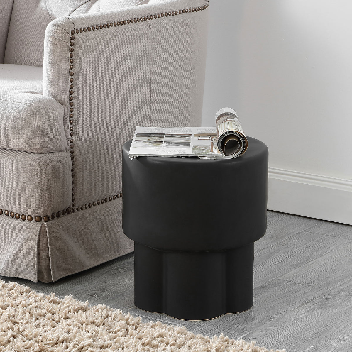 Matte black ceramic stool doubles as a sleek side table beside upholstered seating