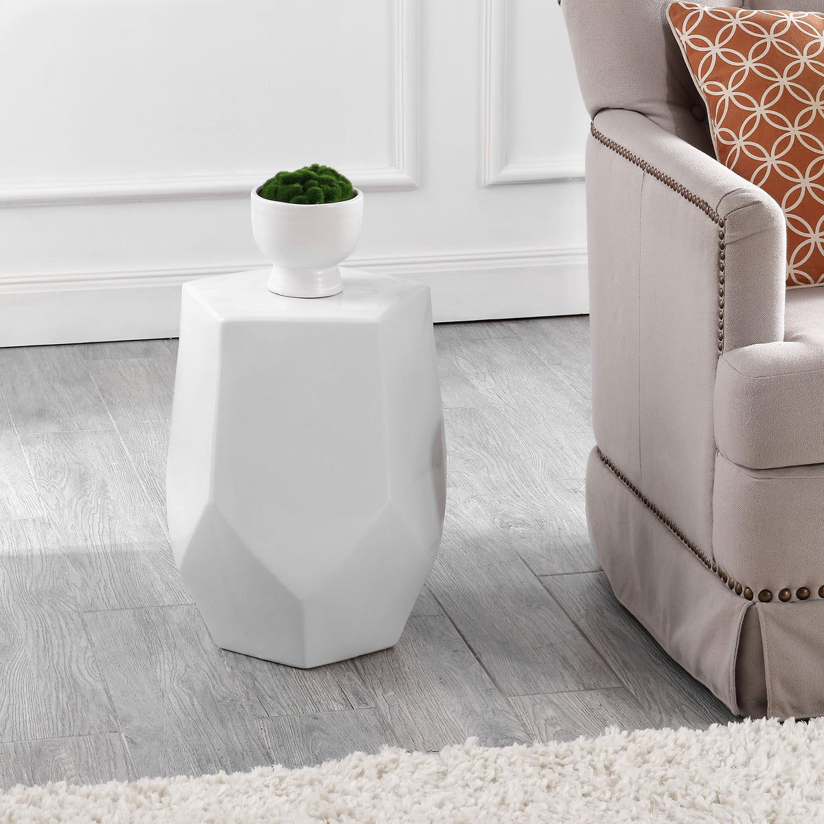 A sculpted white ceramic stool holds a potted plant beside an upholstered chair || ACS4596A || front_angle_room