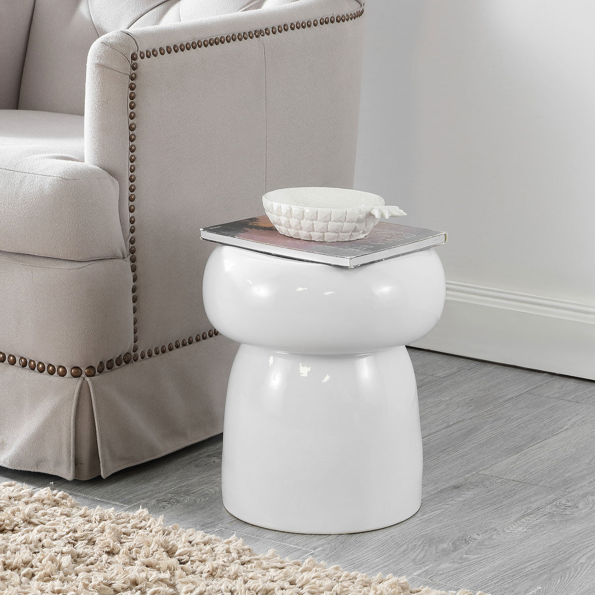 The white ceramic garden stool adds a compact side-table surface beside a cozy chair. || ACS4598A || front_room
