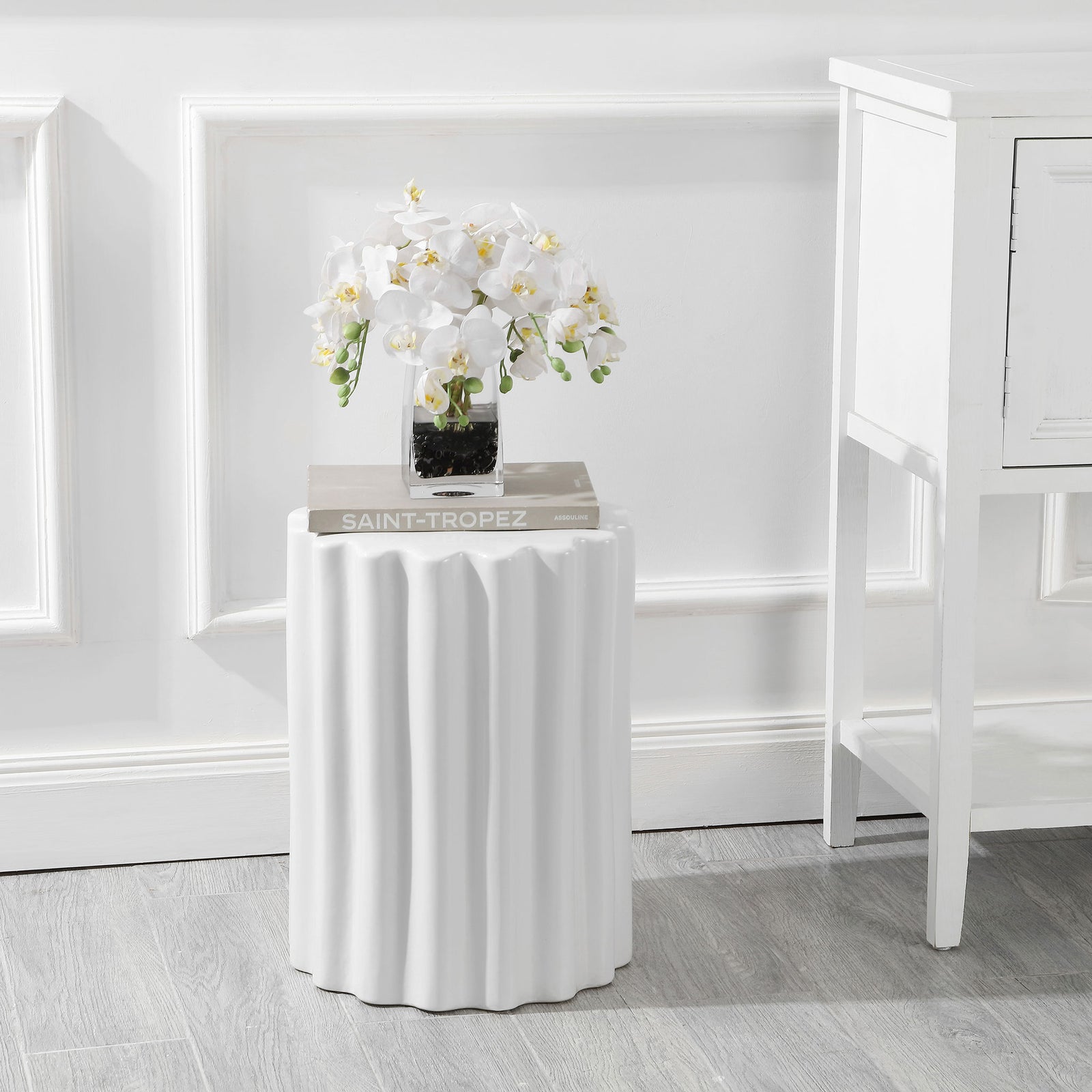 White fluted ceramic stool serves as a graceful side table for books and flowers || ACS4600A || front_angle_room