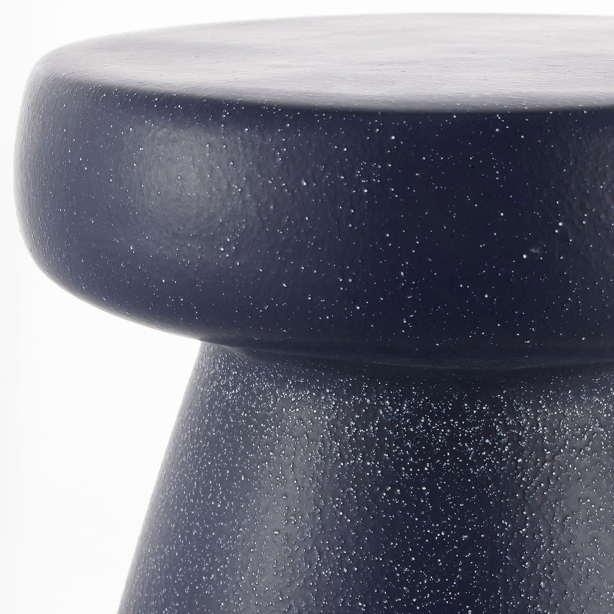 Rounded navy top and narrow waist display the ceramic stool's scattered speckles