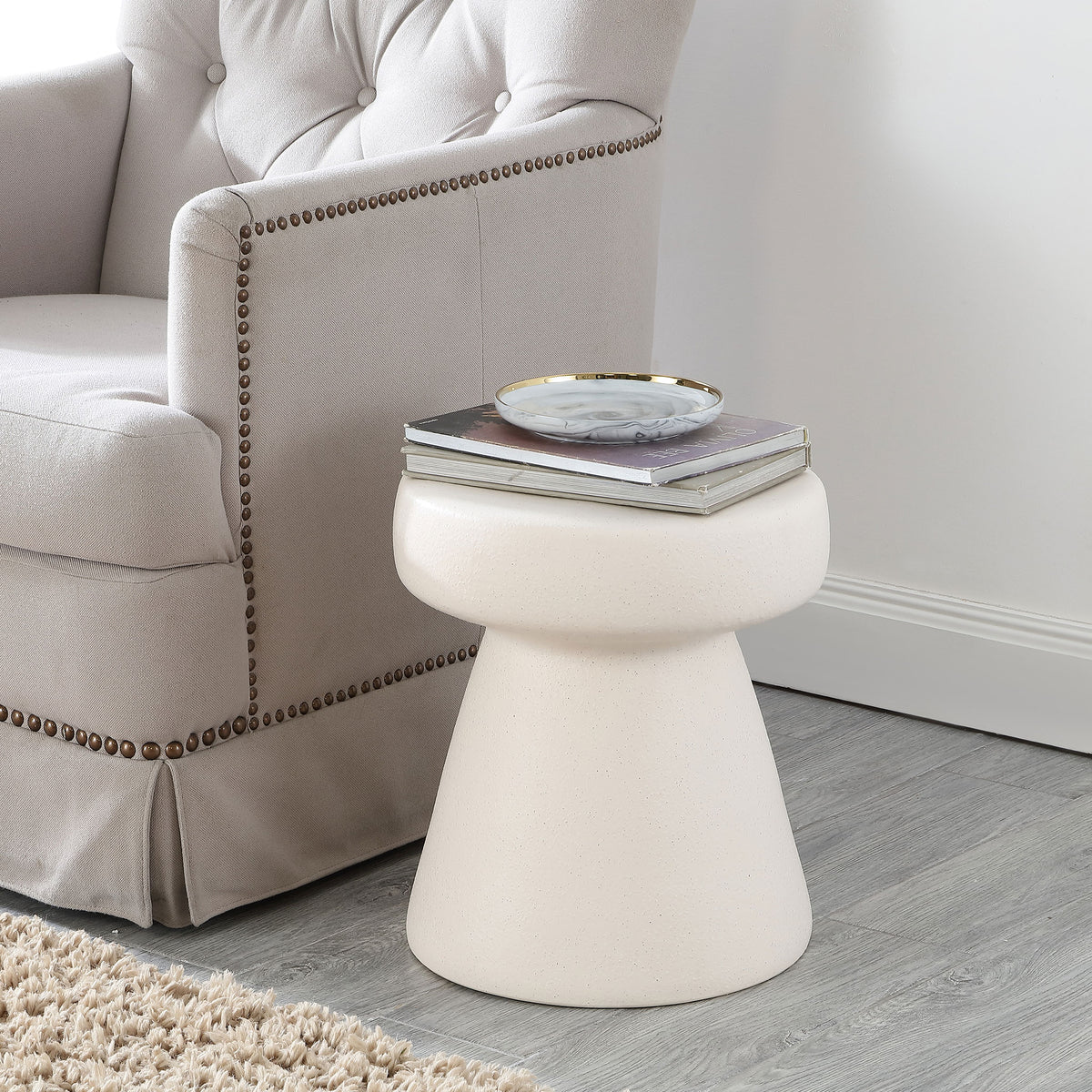 Cream ceramic stool serves as a compact side table beside a tufted armchair
