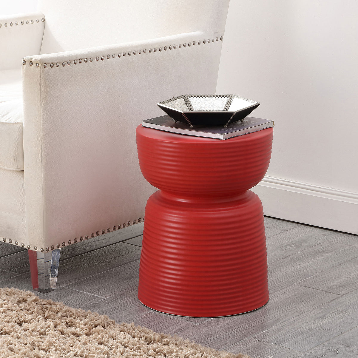 Bright red ribbed ceramic stool serves as a compact side table beside an upholstered chair