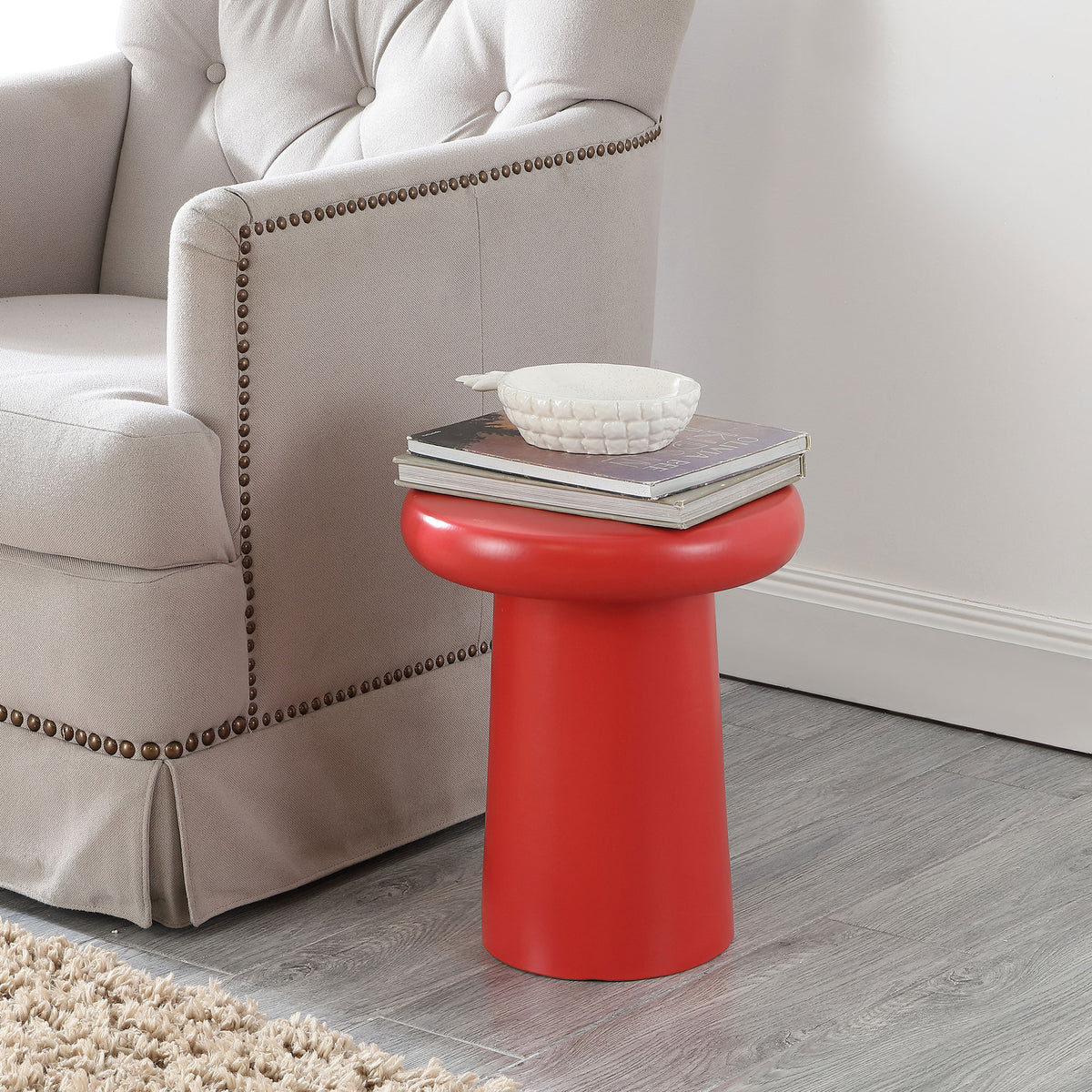 A bright red ceramic stool serves as a compact side table beside an upholstered chair.