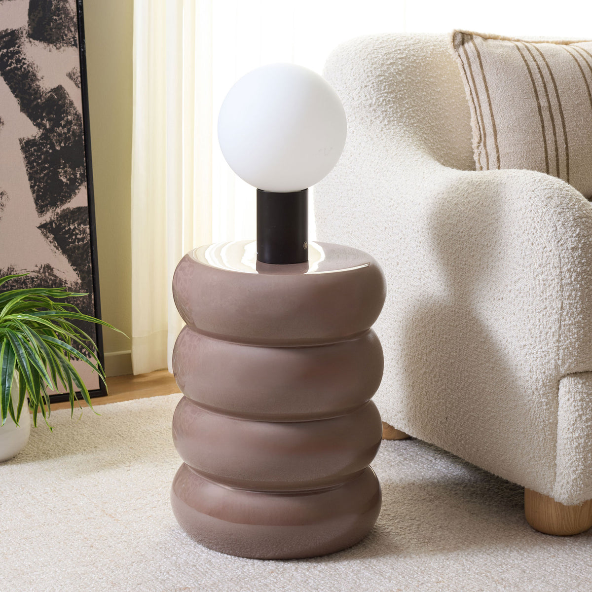 Glossy taupe garden stool serves as a sculptural side table for a lamp beside an armchair.