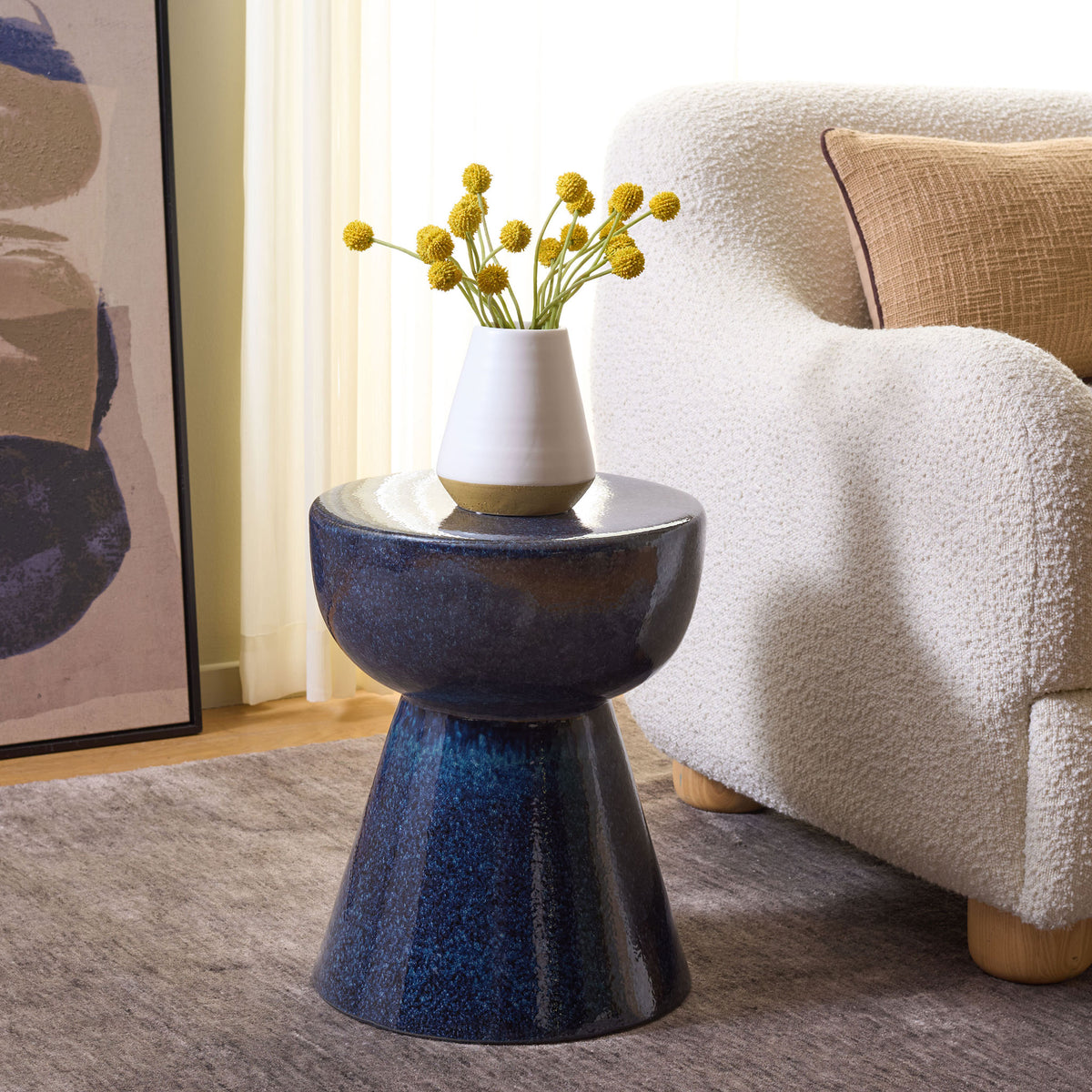 A blue ceramic stool serves as a petite table for flowers beside a cozy chair. || ACS4611B || front_angle_room