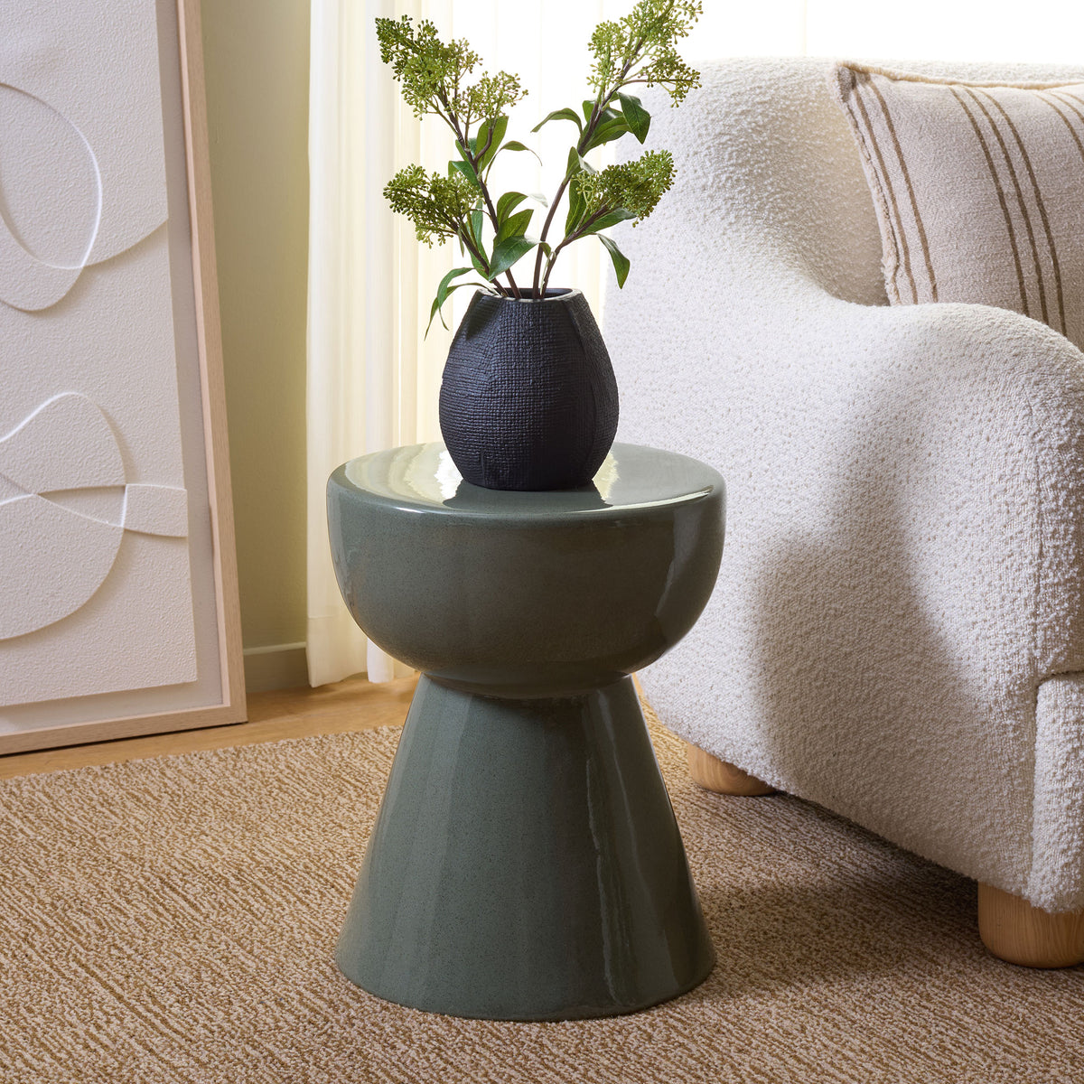 A muted green ceramic stool holds a flower vase beside a cozy white chair. || ACS4611C || front_angle_room