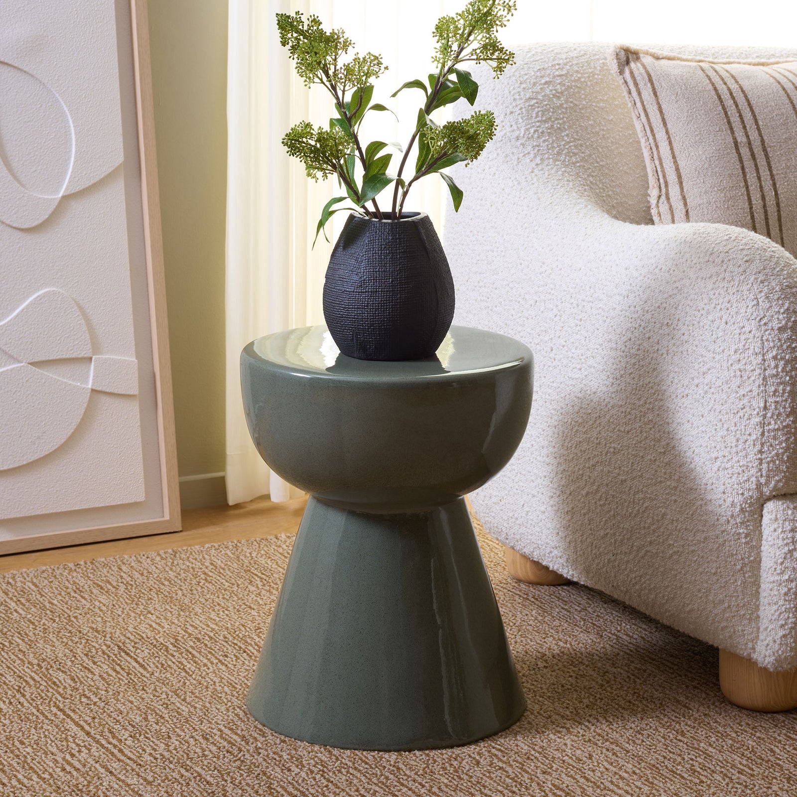 A muted green ceramic stool holds a flower vase beside a cozy white chair. || ACS4611C || front_angle_room