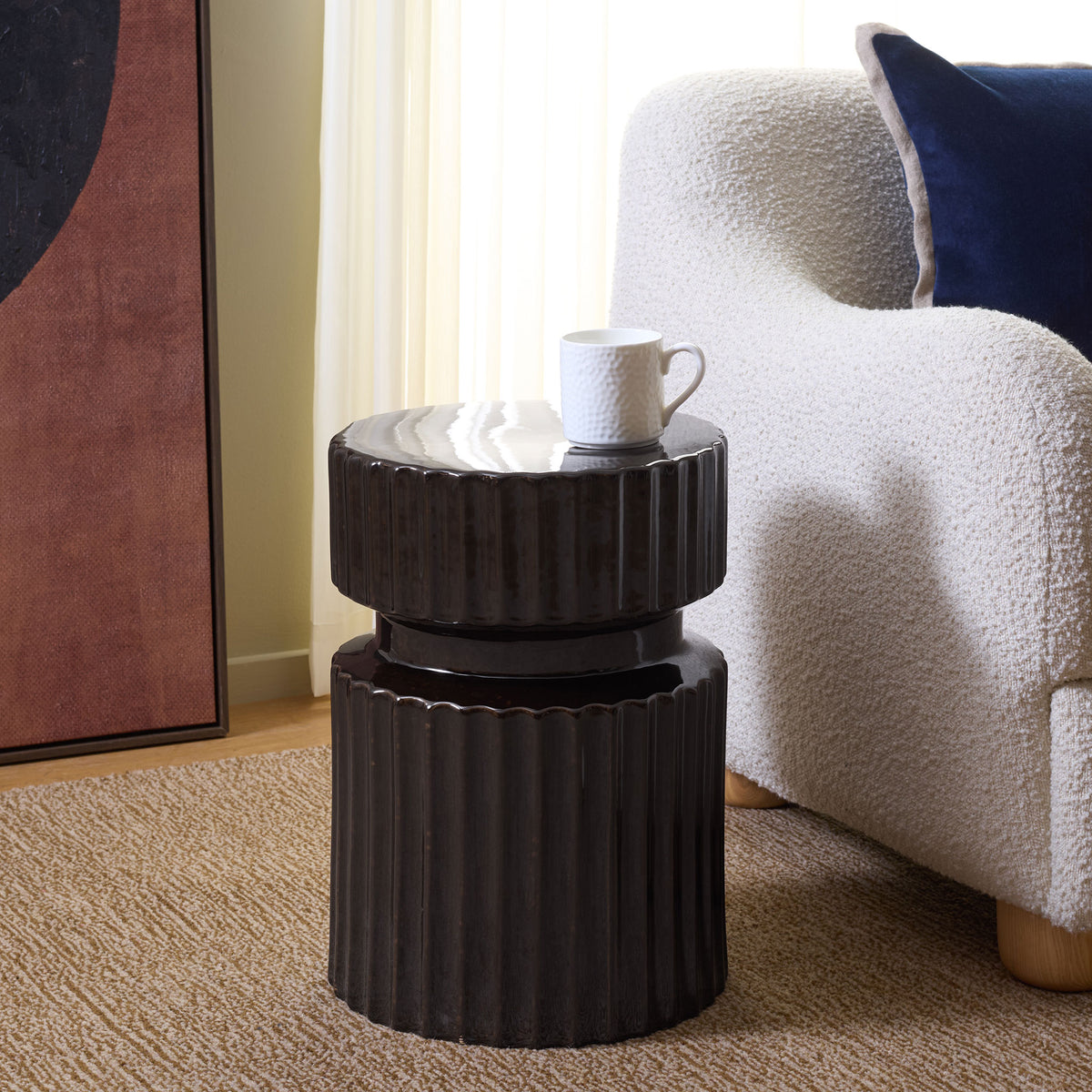 A fluted brown ceramic stool doubles as a side table beside a cozy chair.