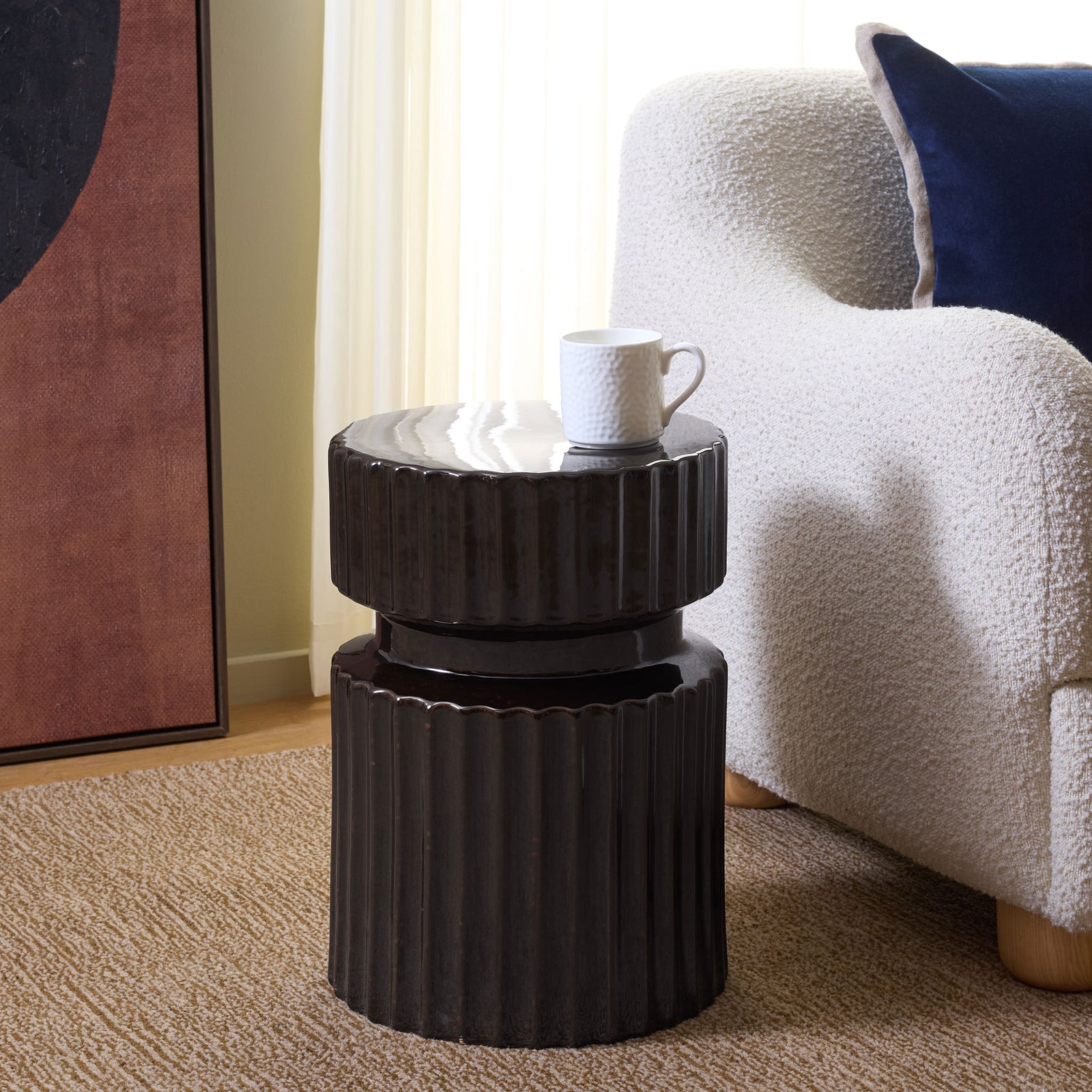 A fluted brown ceramic stool doubles as a side table beside a cozy chair. || ACS4613A || front_angle_room