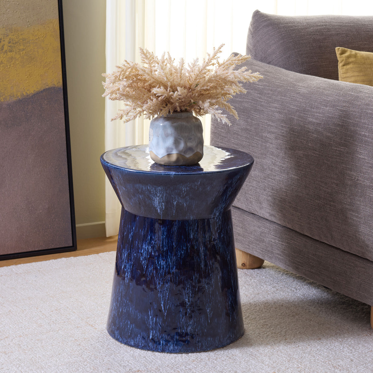 Sculptural blue ceramic stool doubles as a side table beside a sofa, with a round top for a vase || ACS4615A || front_angle_room