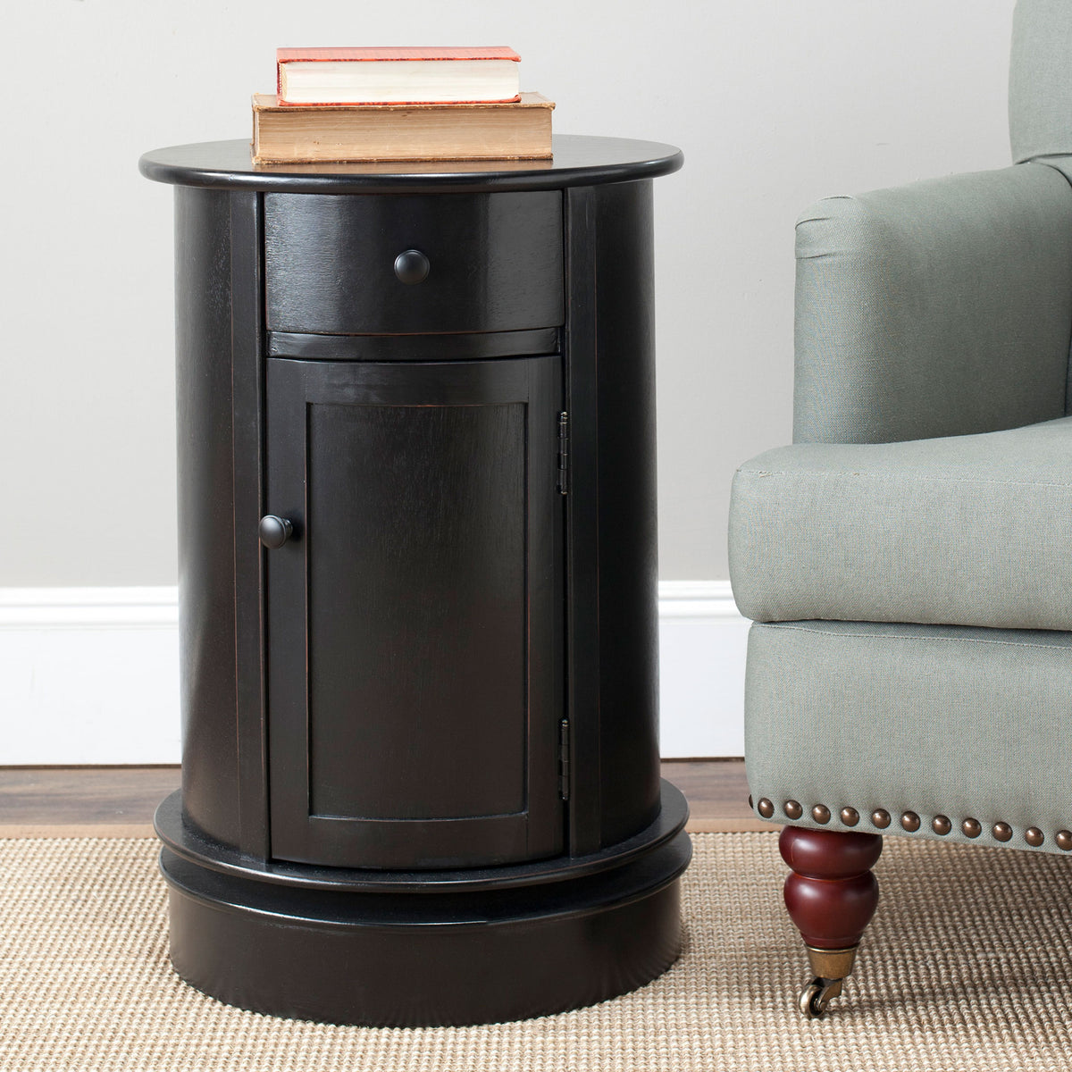 Books rest on a distressed black round table next to an upholstered armchair