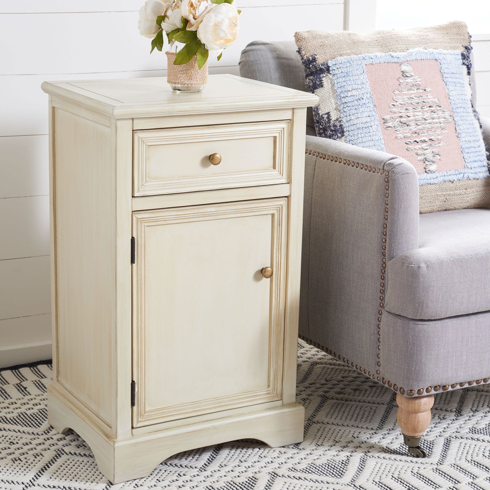 Cream nightstand lends concealed storage and vintage warmth beside an upholstered chair || AMH6627D || front_angle_room