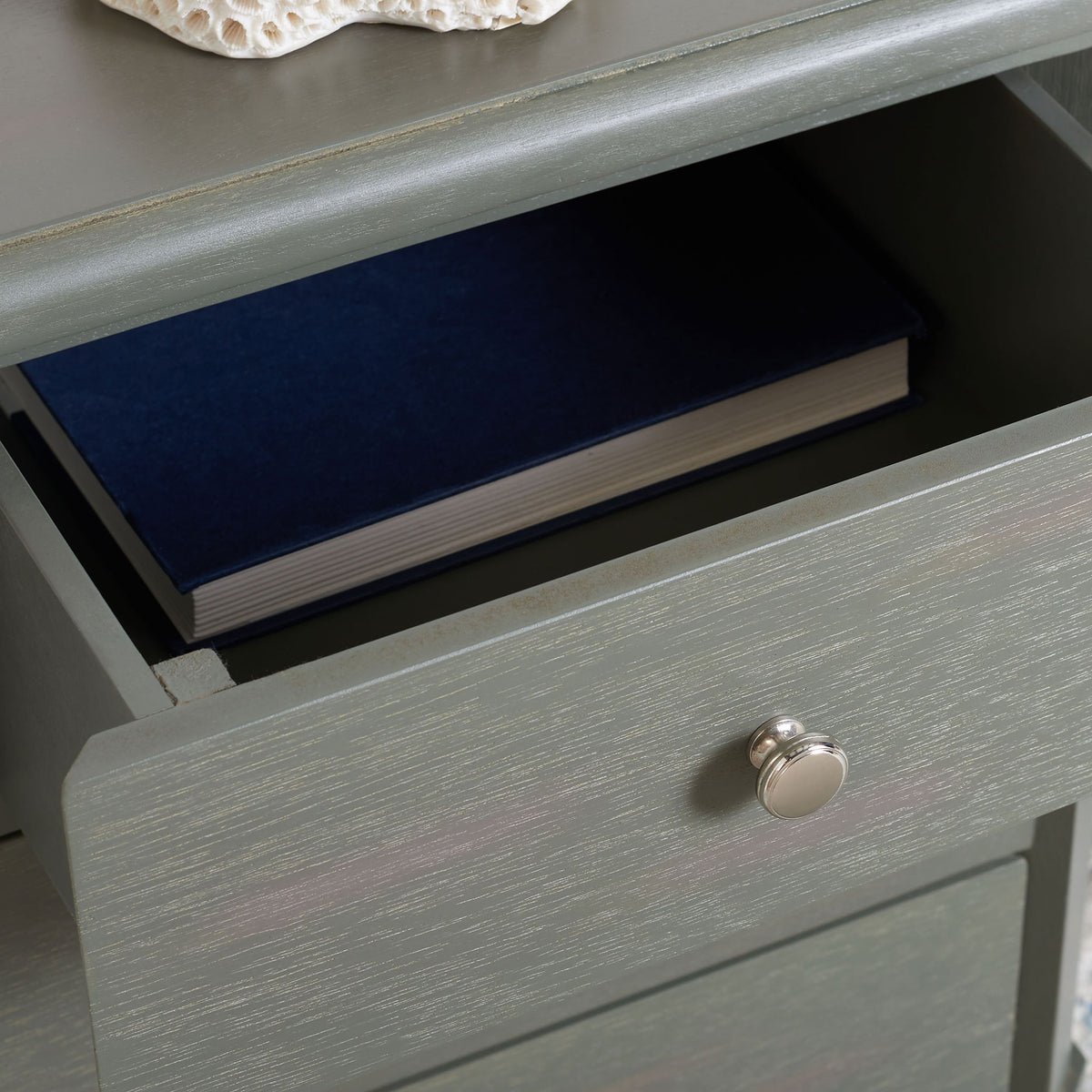 An open drawer holds a favorite book beneath the softly beveled gray tabletop.
