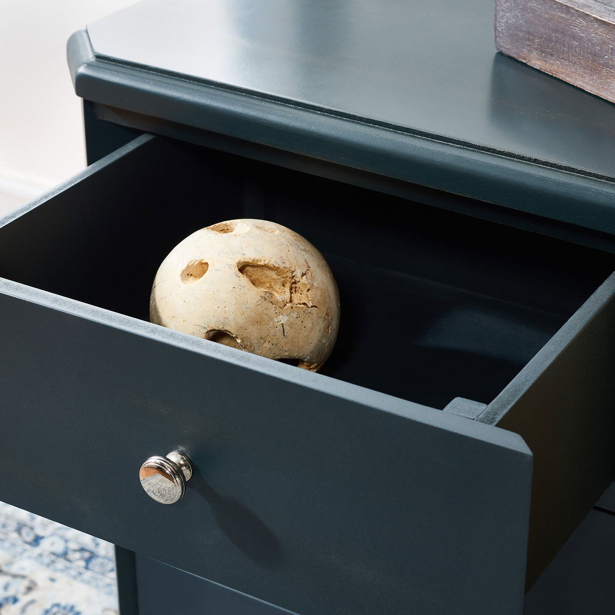 An open drawer in dark teal wood keeps small treasures close with a shiny silver knob.
