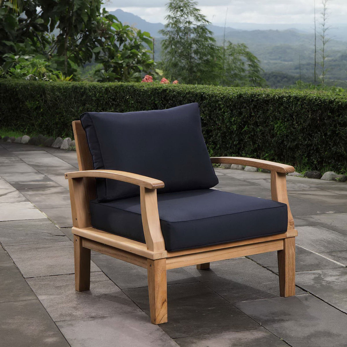 Marina teak armchair with navy cushions arranged on a contemporary stone patio || EEI-1143-NAT-NAV-SET || front_angle_room