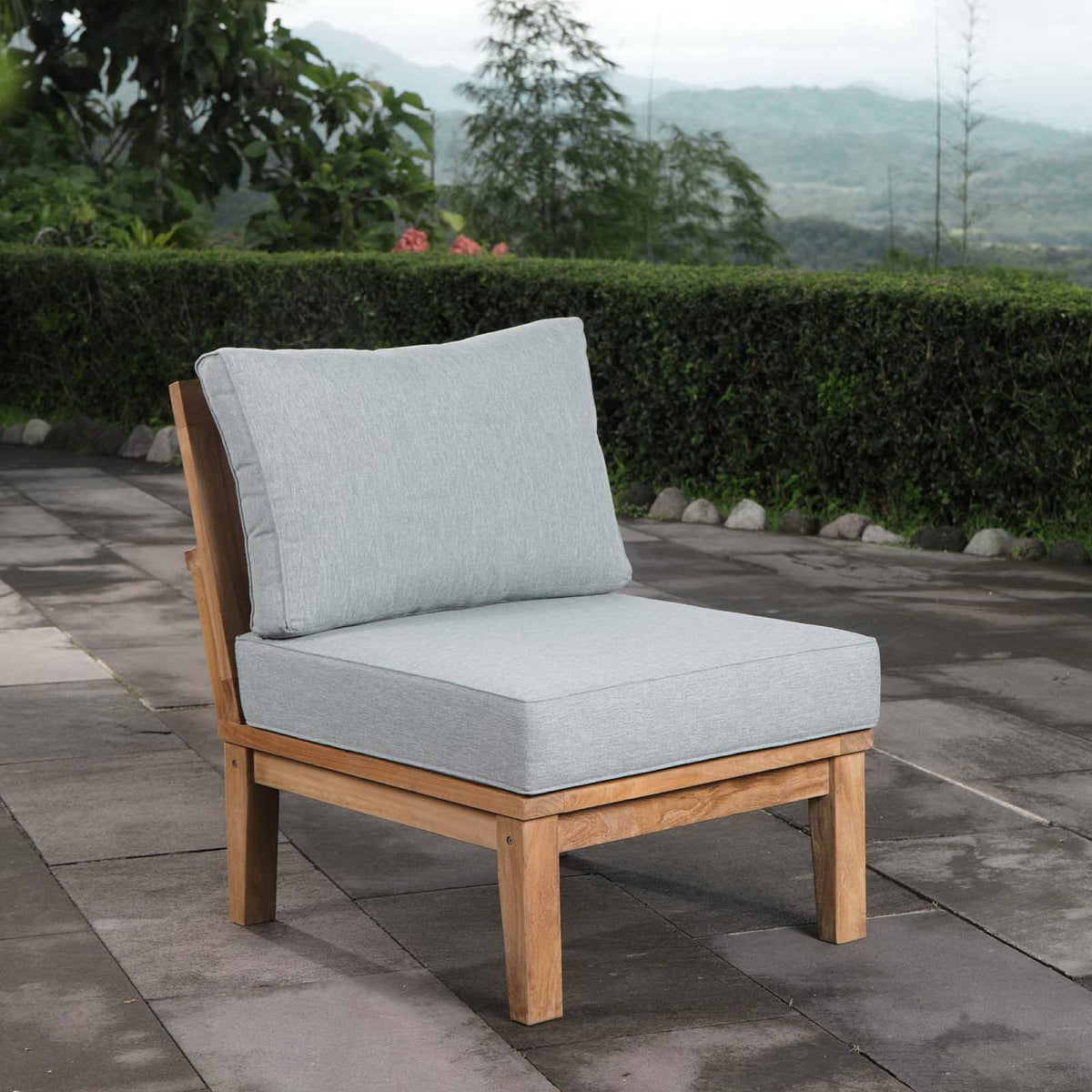 Marina armless teak chair with gray cushions placed along a scenic garden patio || EEI-1150-NAT-GRY-SET || front_angle_room