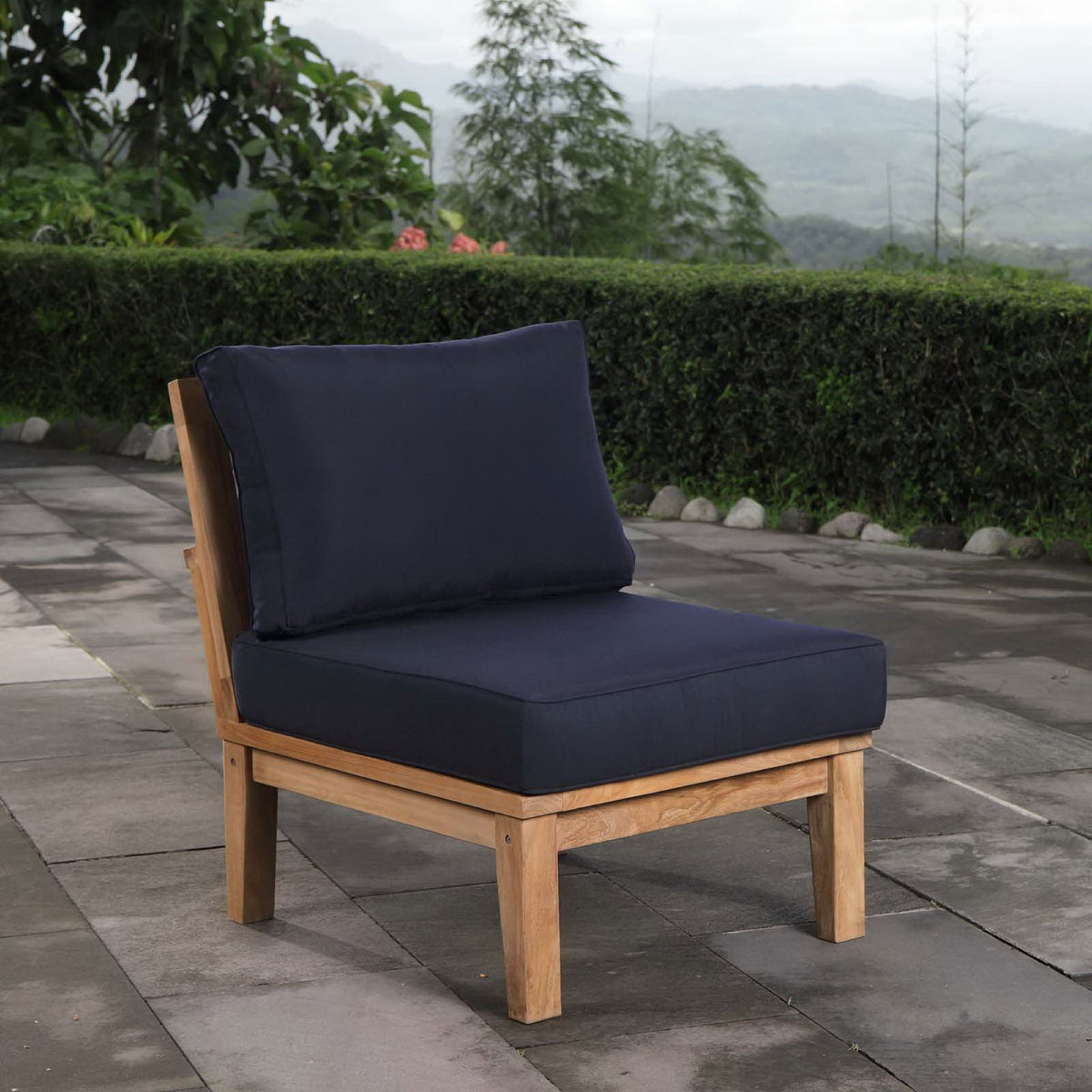 Marina armless teak chair with navy cushions arranged on a stone terrace || EEI-1150-NAT-NAV-SET || front_angle_room