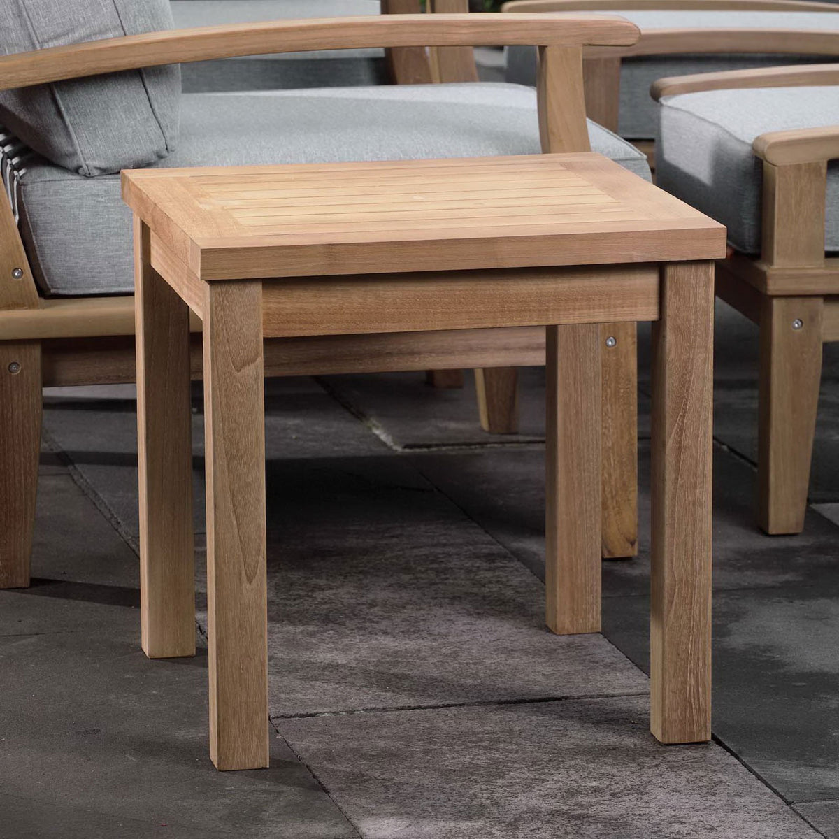 Marina natural teak side table styled with matching lounge seating on a modern outdoor patio. || EEI-1155-NAT || front_angle_room