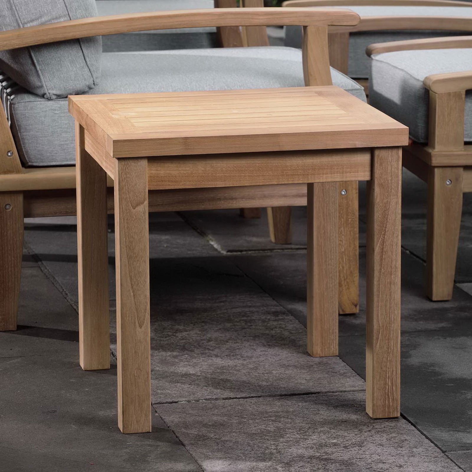 Marina natural teak side table styled with matching lounge seating on a modern outdoor patio. || EEI-1155-NAT || front_angle_room
