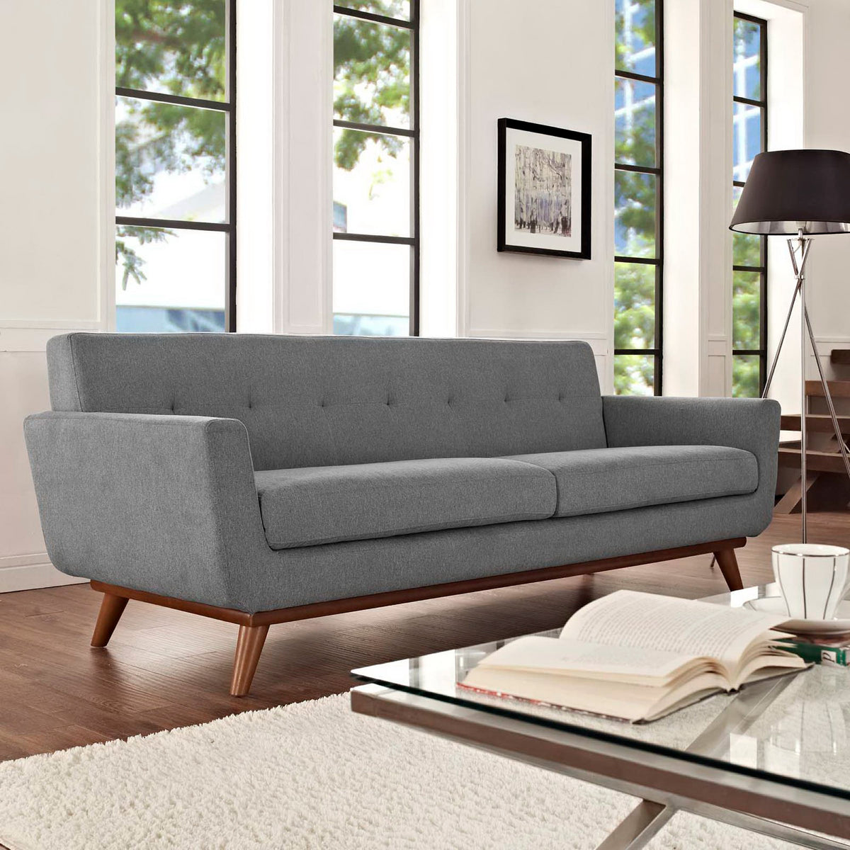 Gray sofa pairs a button-tufted back and plush cushions with mid-century wood legs