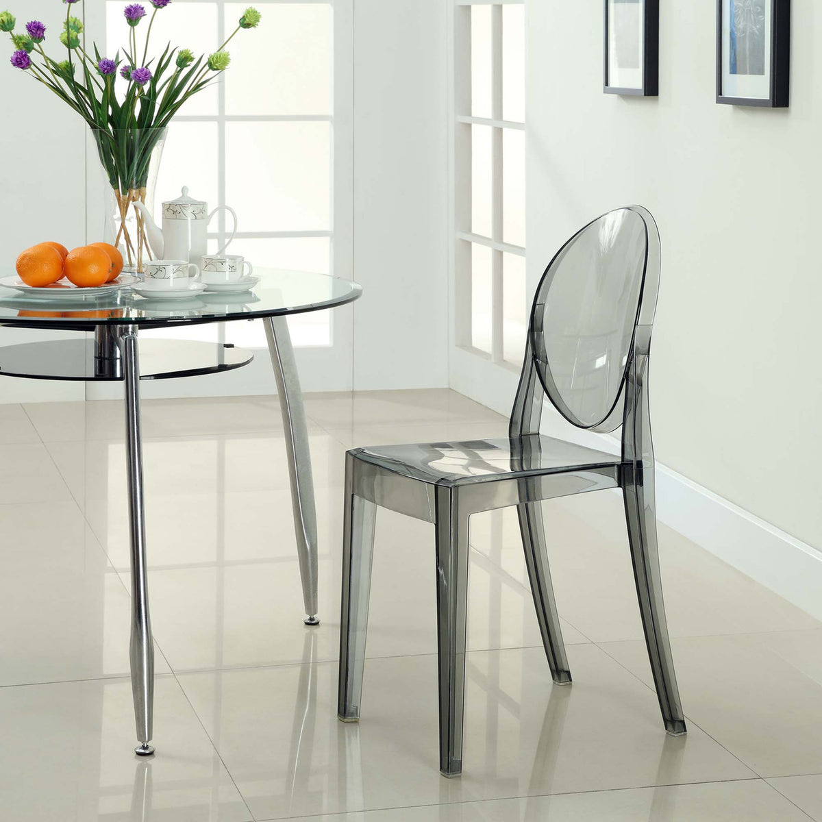 Smoky transparent chair balances an oval back and slim legs beside a glass dining table