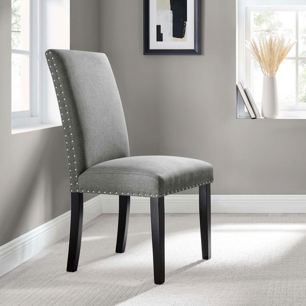 Parcel light gray upholstered dining chair with nailhead trim styled in a contemporary neutral dining nook. || EEI-1384-LGR || front_angle_room