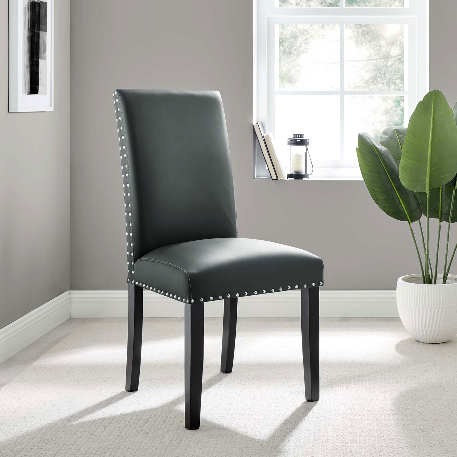 Gray faux leather dining chair with nailhead trim styled in a bright modern room with greenery || EEI-1491-GRY || front_angle_room