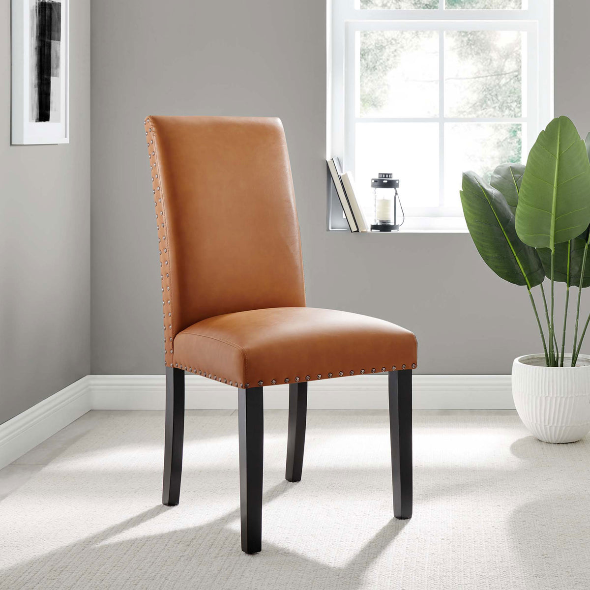 Tan faux leather dining chair with nailhead trim styled in a bright modern room || EEI-1491-TAN || front_angle_room