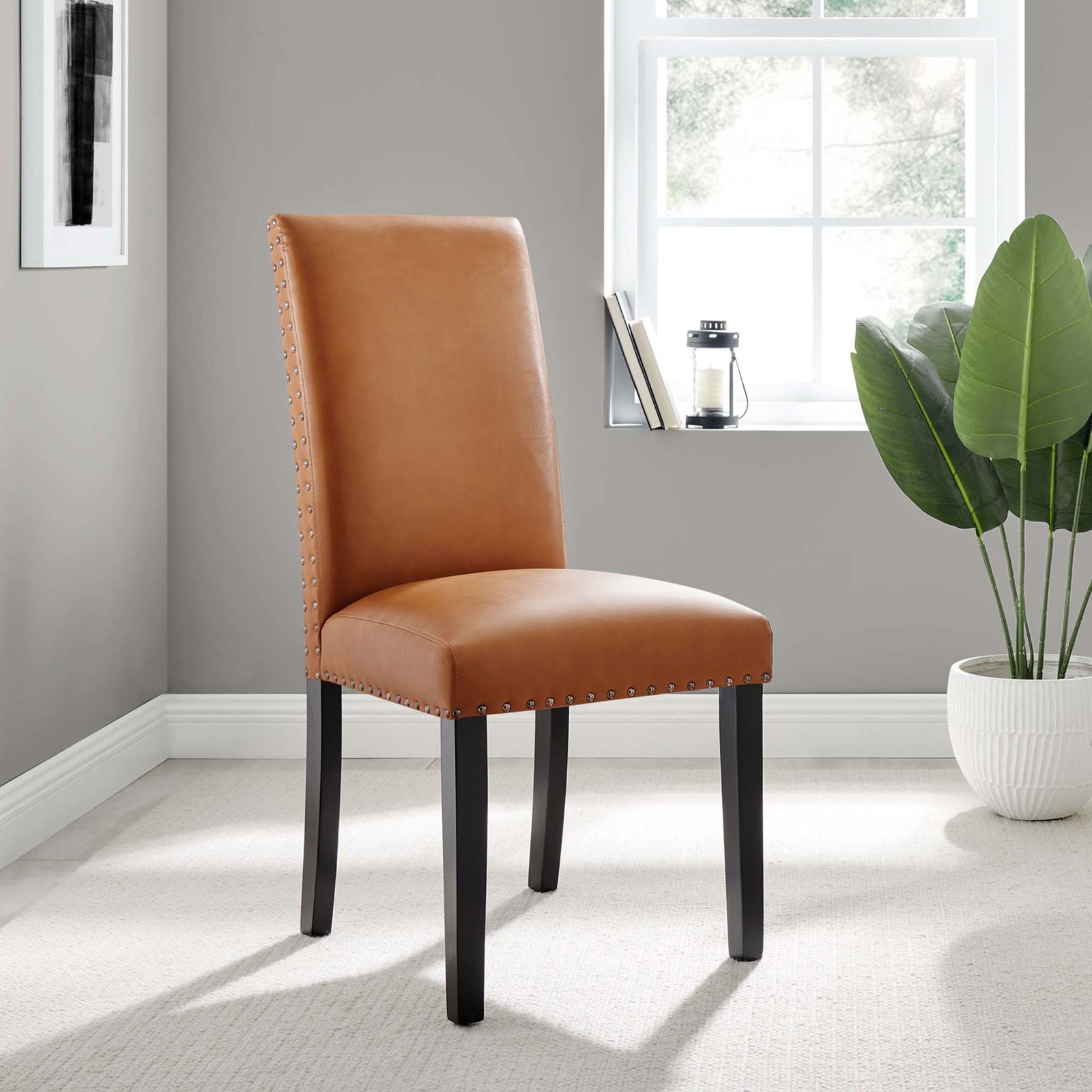Tan faux leather dining chair with nailhead trim styled in a bright modern room || EEI-1491-TAN || front_angle_room