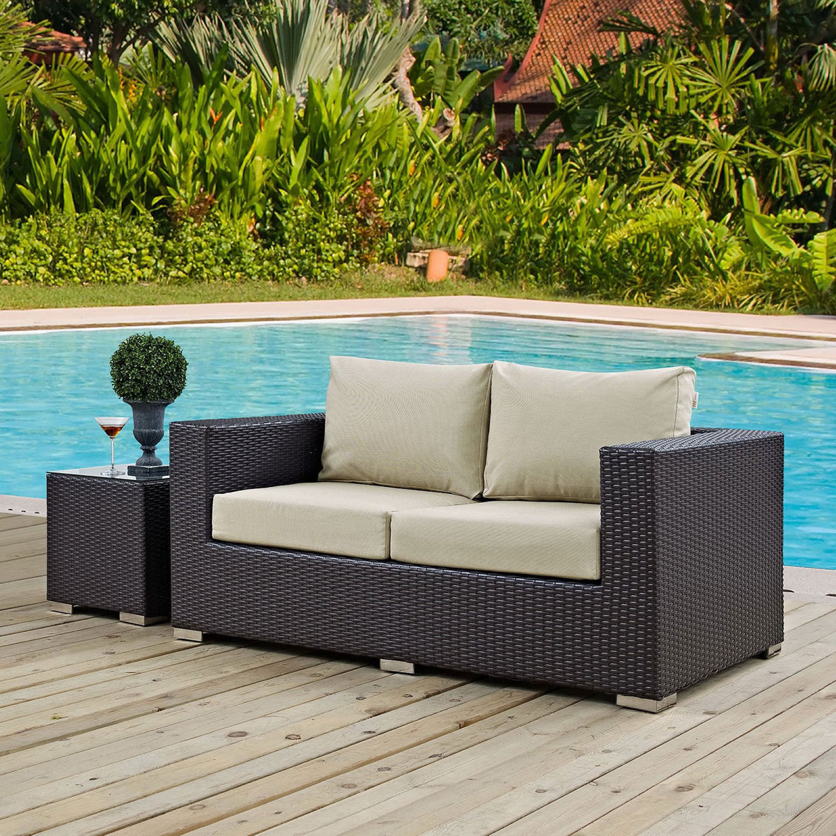 Espresso outdoor loveseat with beige cushions sits beside the pool, styled with greenery and a side table || EEI-1907-EXP-BEI || front_angle_room