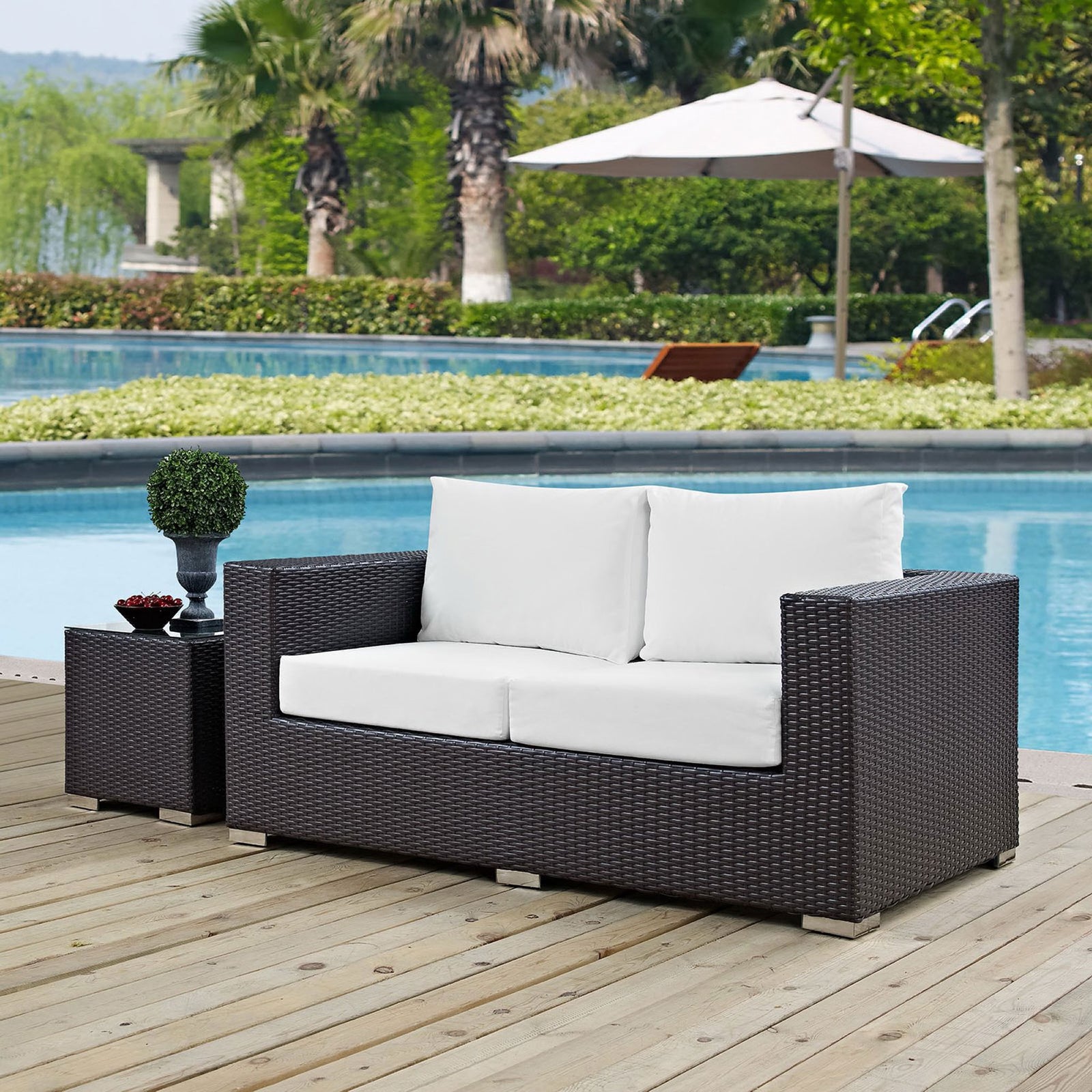 Espresso outdoor loveseat with white cushions overlooks the pool, framed by lush landscaping and wood decking || EEI-1907-EXP-WHI || front_angle_room