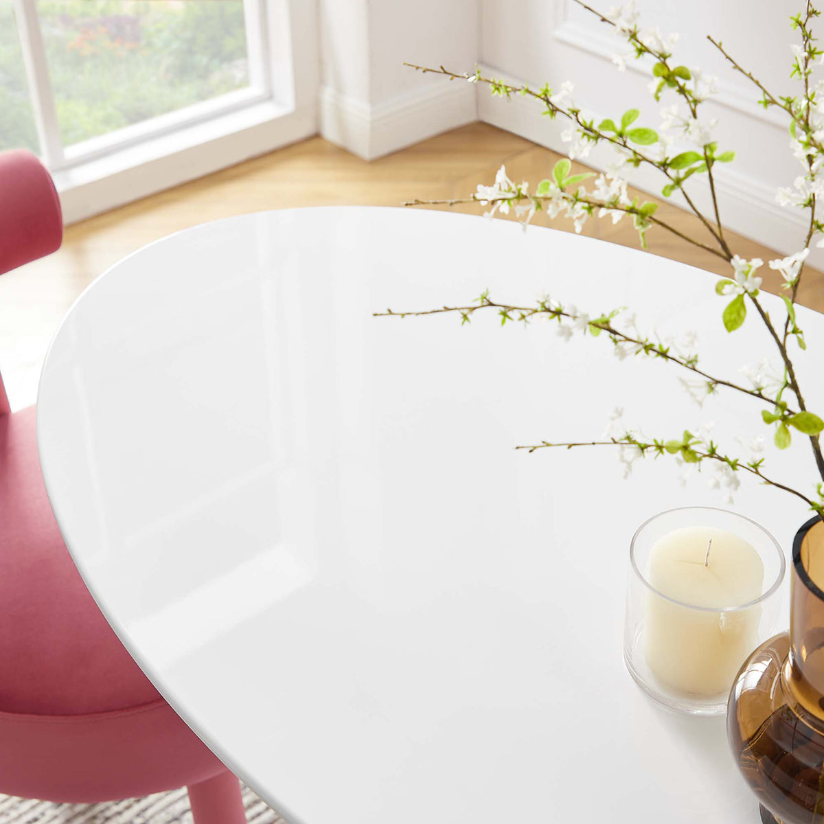 Glossy white 48-inch oval tabletop styled with a branch-filled vase and candle in a sunlit dining room