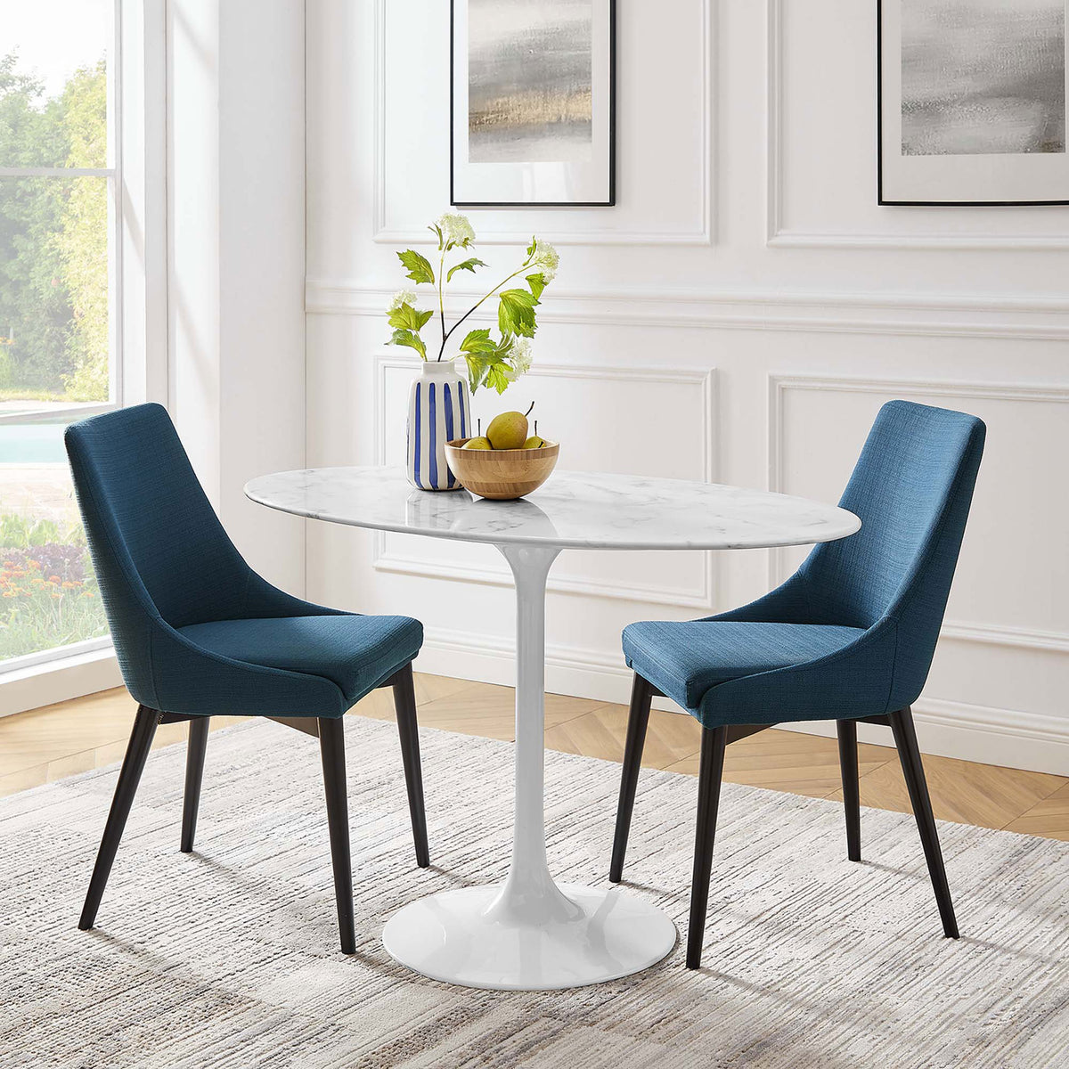 Oval faux marble dining table anchors a bright white dining room with plush blue chairs and greenery || EEI-2021-WHI || front_room